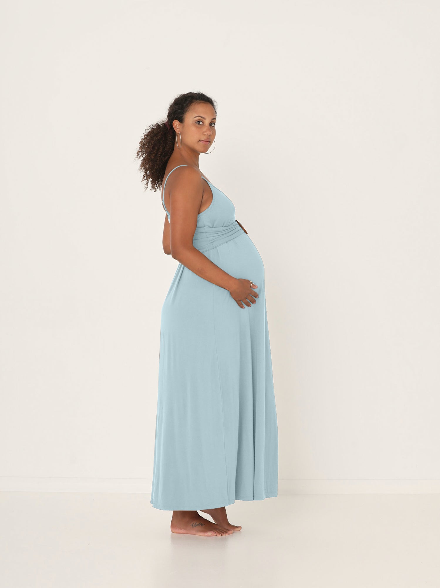 Pregnant woman wearing a light blue bamboo maxi slip dress against a white background