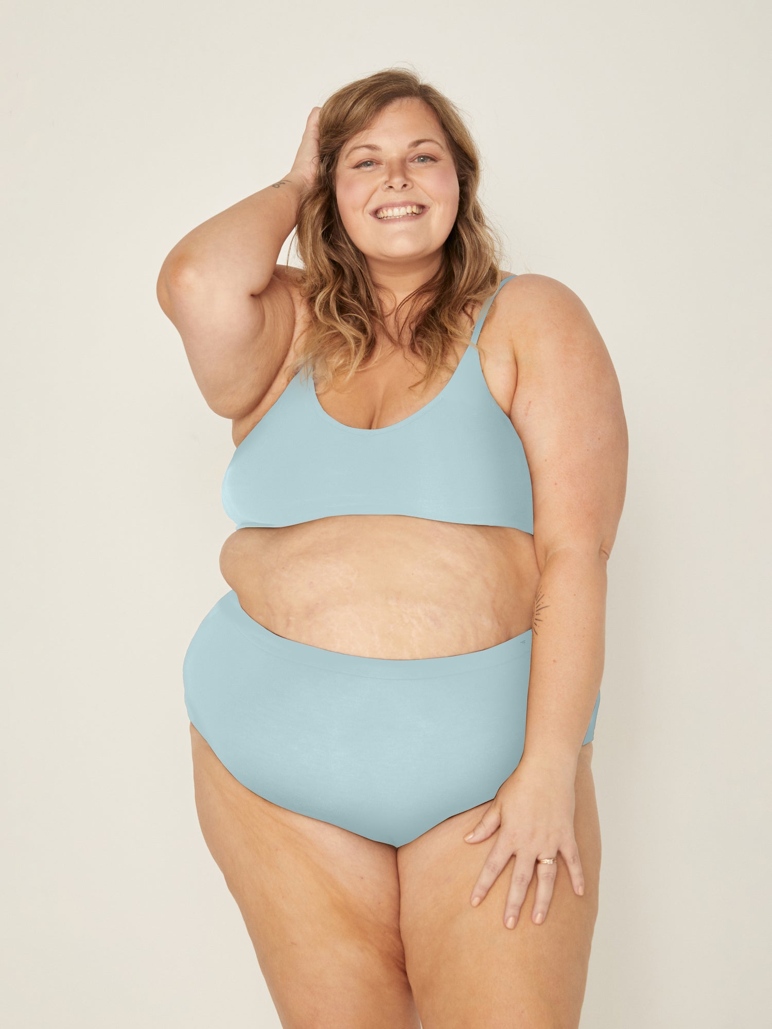 Woman wearing a light blue bralette and knickers set against a plain background