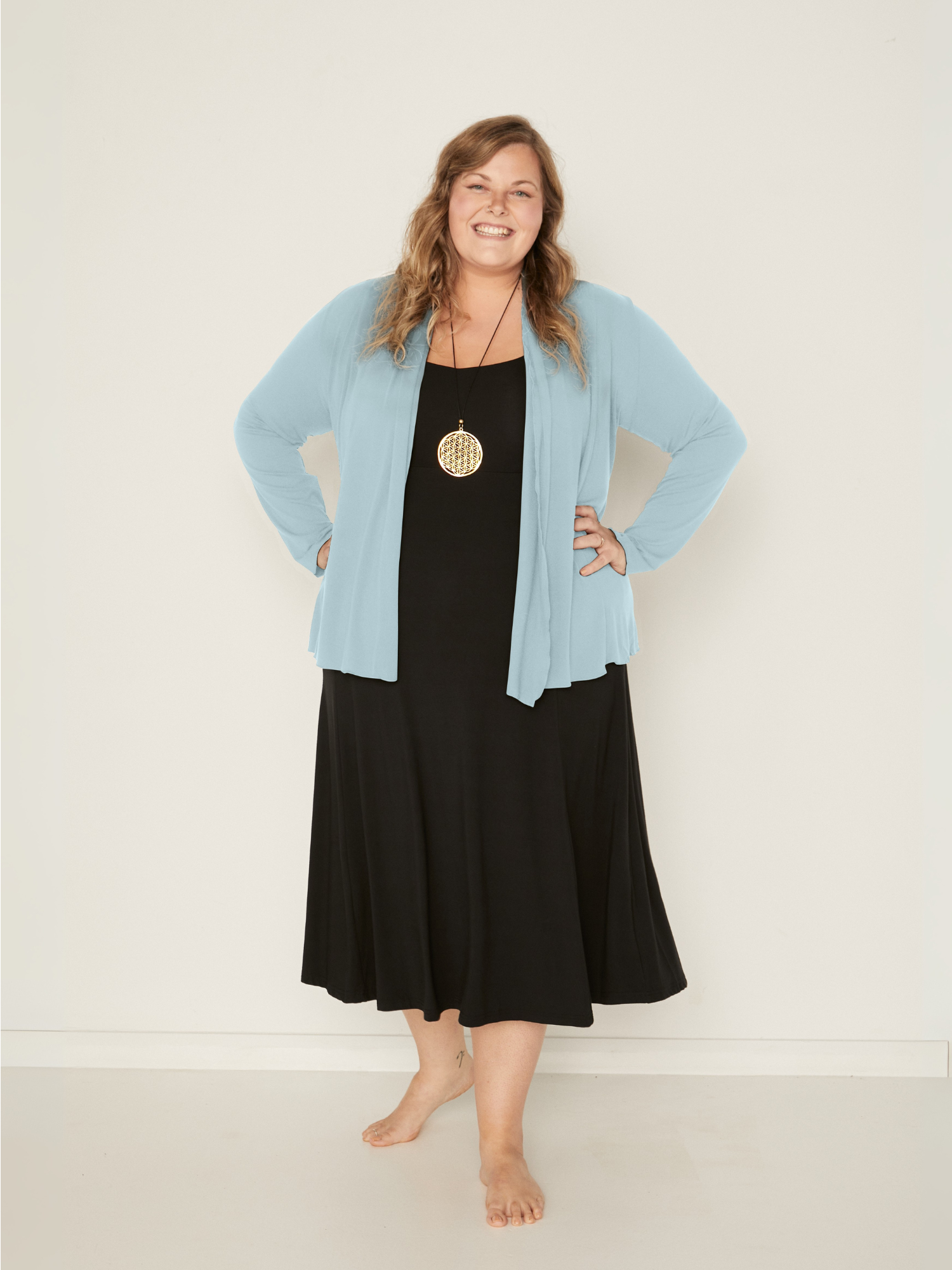 Woman wearing a bamboo topaz blue mid cardigan over a black dress against a white background