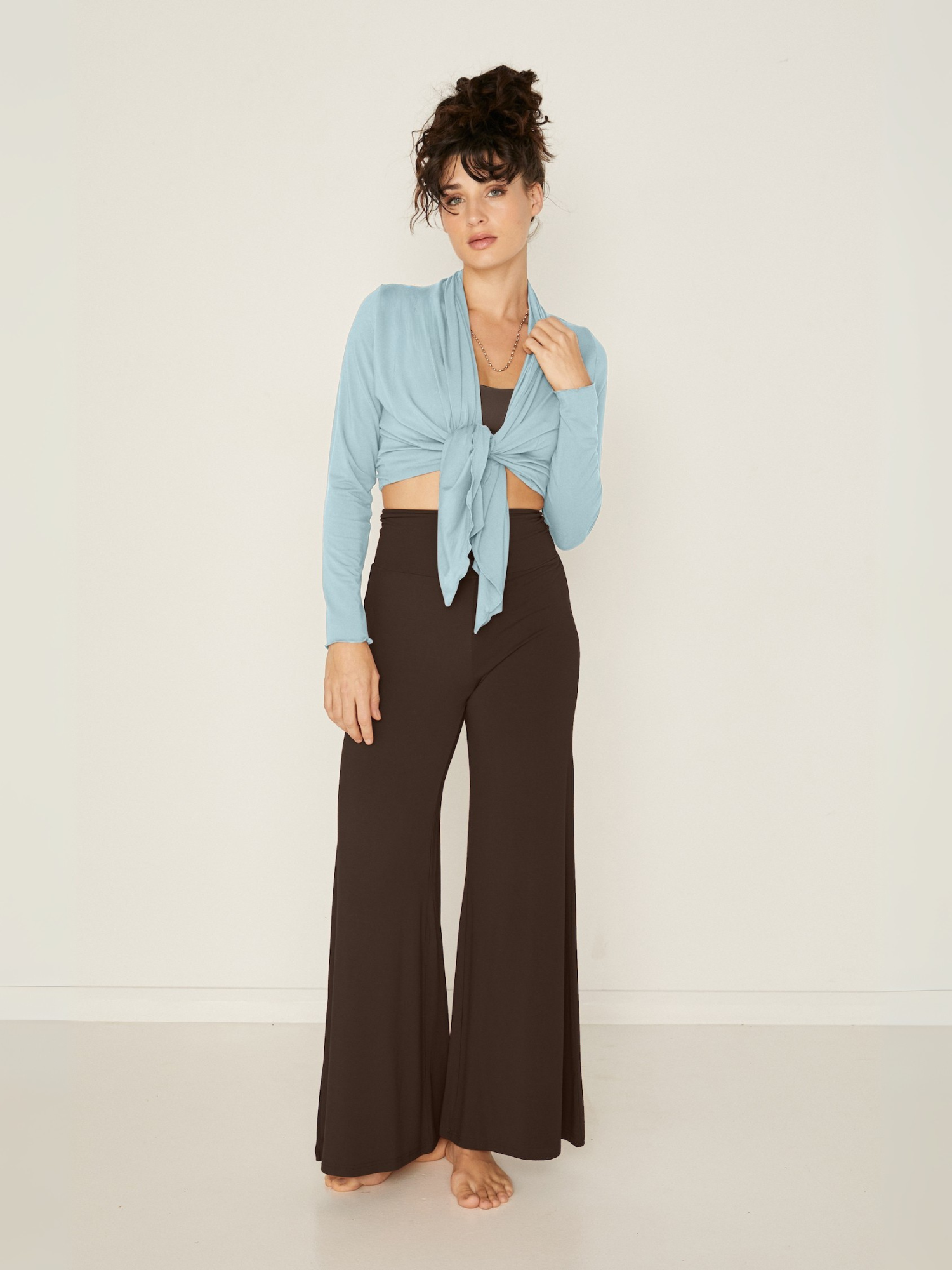 Model wearing cocoa full length palazzo pants, fitted waist and hips with flowing wide leg, adjustable high waistband, with a light topaz blue mid cardigan, women's bamboo clothing