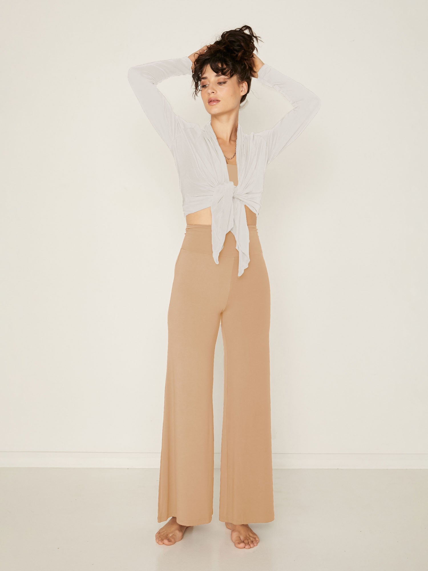 Model wearing caramel full length palazzo pants, fitted waist and hips with flowing wide leg, adjustable high waistband, women's bamboo clothing
