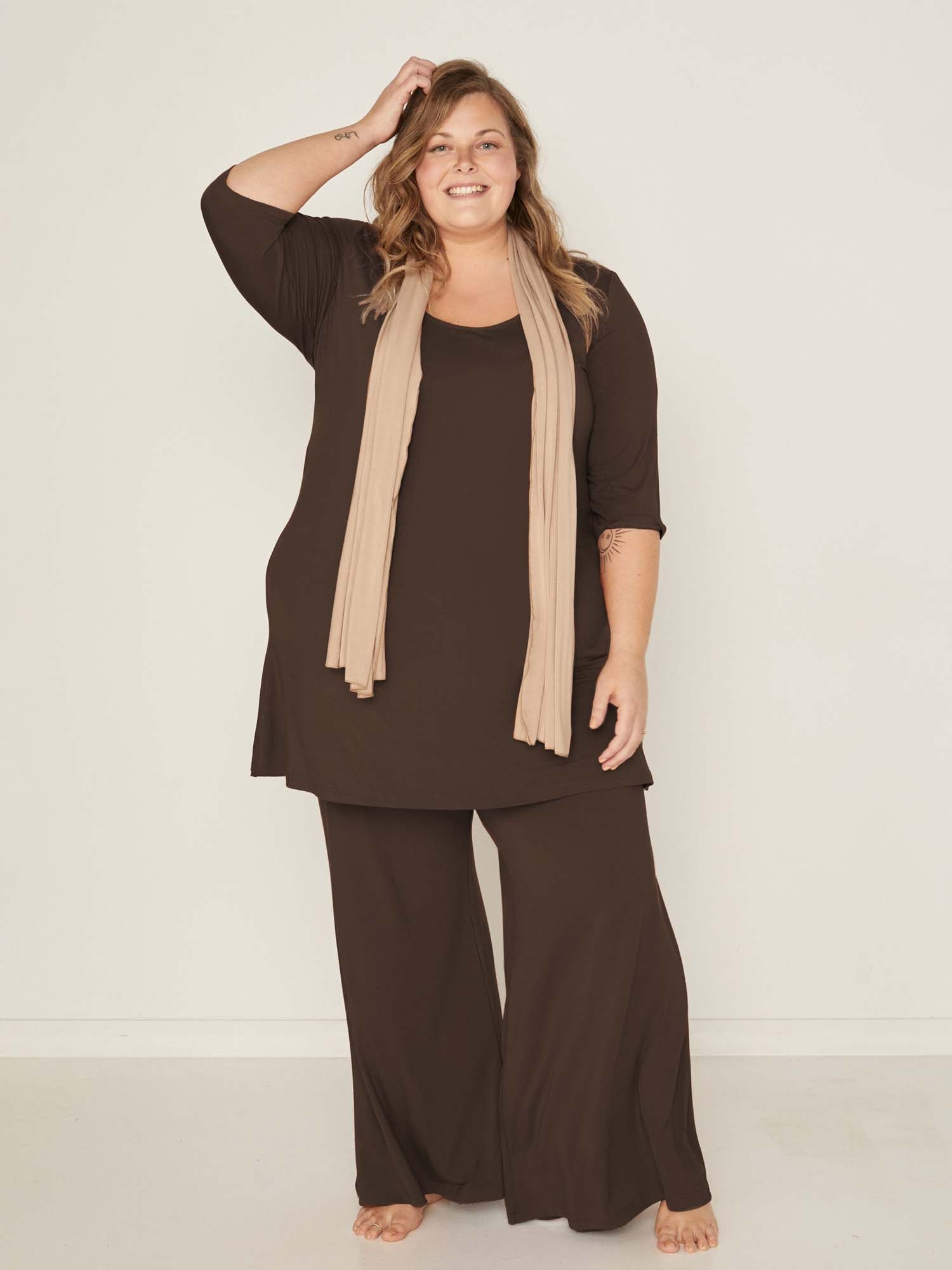Model wearing cocoa full length palazzo pants, fitted waist and hips with flowing wide leg, adjustible high waistband, women's bamboo clothing