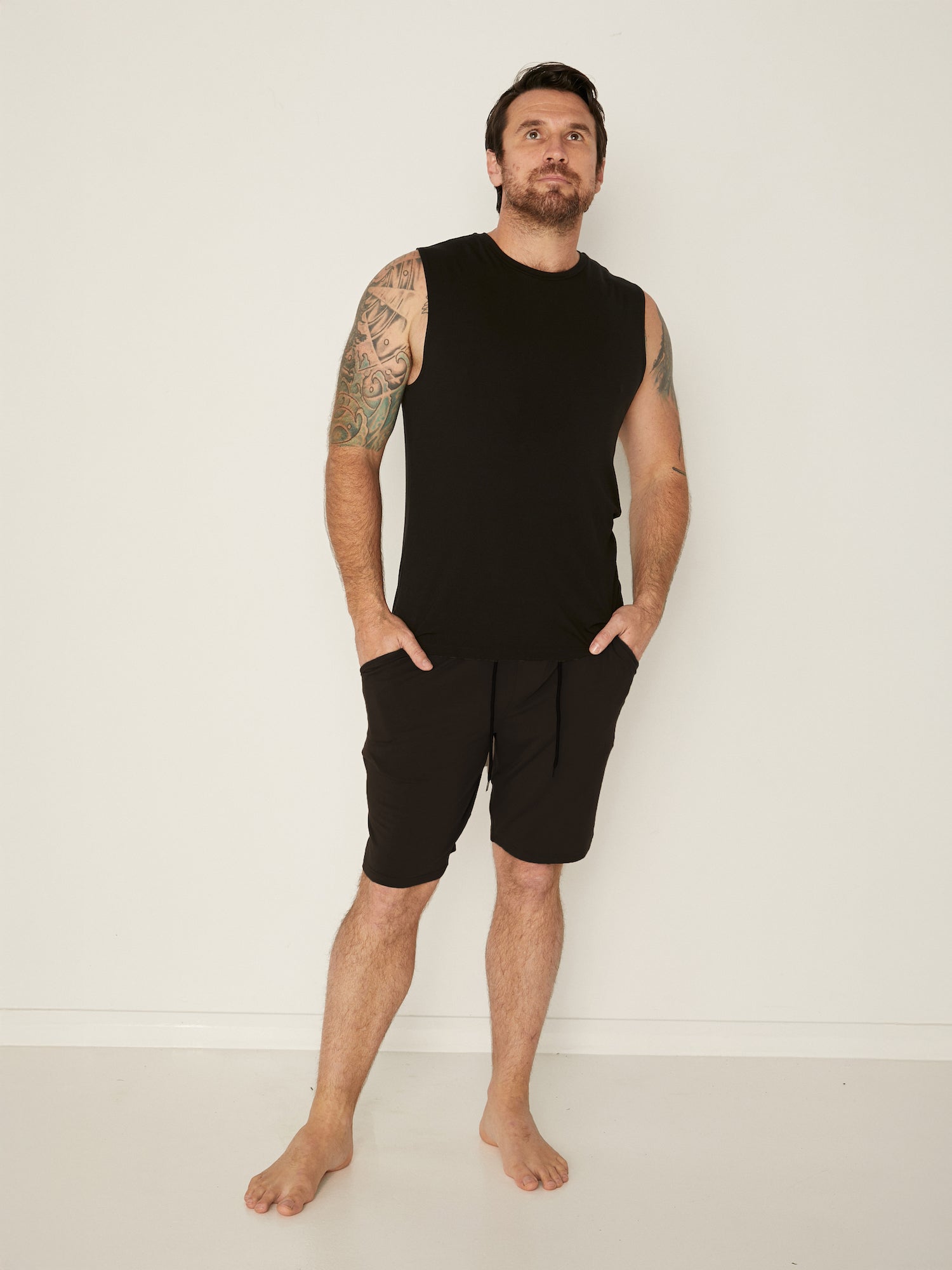Male model wearing black generous classic fit tank singlet, soft neckband, crew neckline, sleeveless, men's bamboo clothing