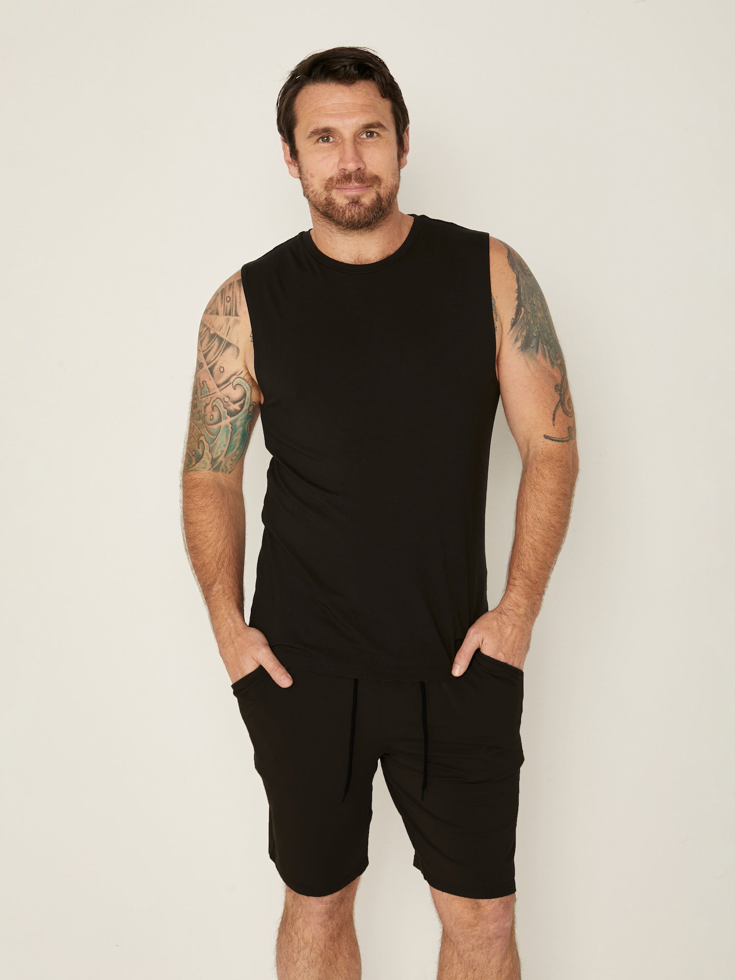 Male model wearing black generous classic fit tank singlet, soft neckband, crew neckline, sleeveless, men's bamboo clothing