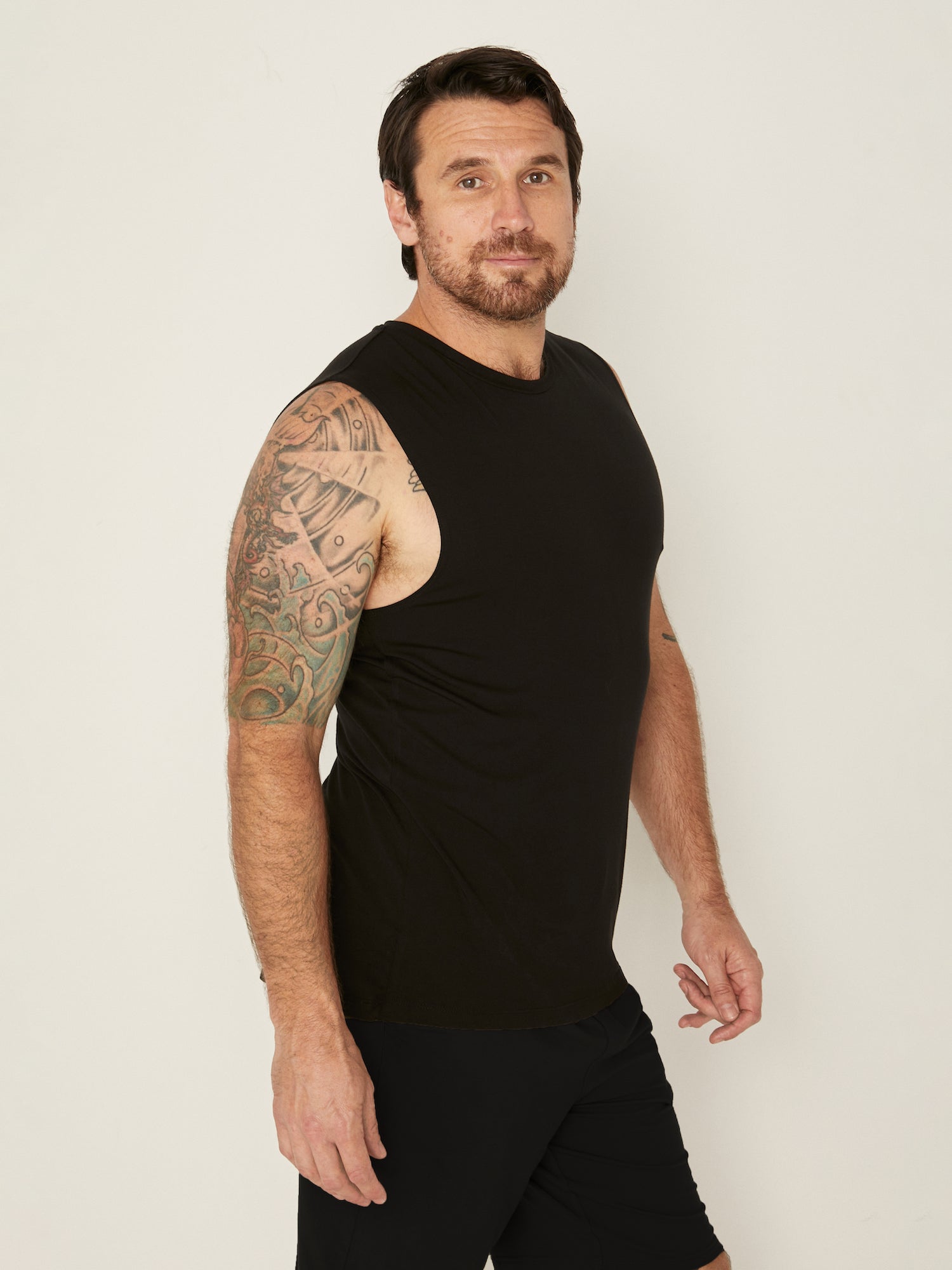 Male model wearing black generous classic fit tank singlet, soft neckband, crew neckline, sleeveless, men's bamboo clothing