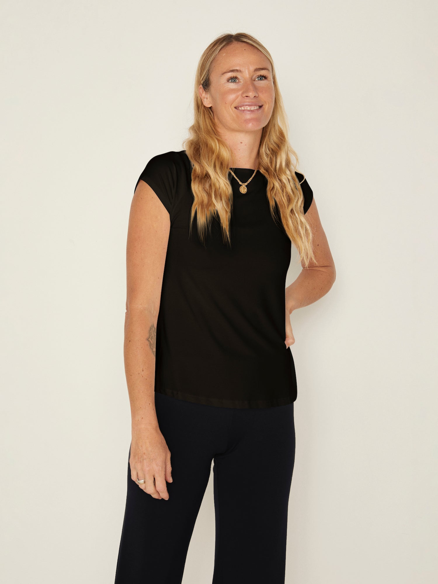 Model wearing a black boat neck t-shirt with capped sleeves, fitted through shoulders and chest with slight flare at waist, women's bamboo clothing