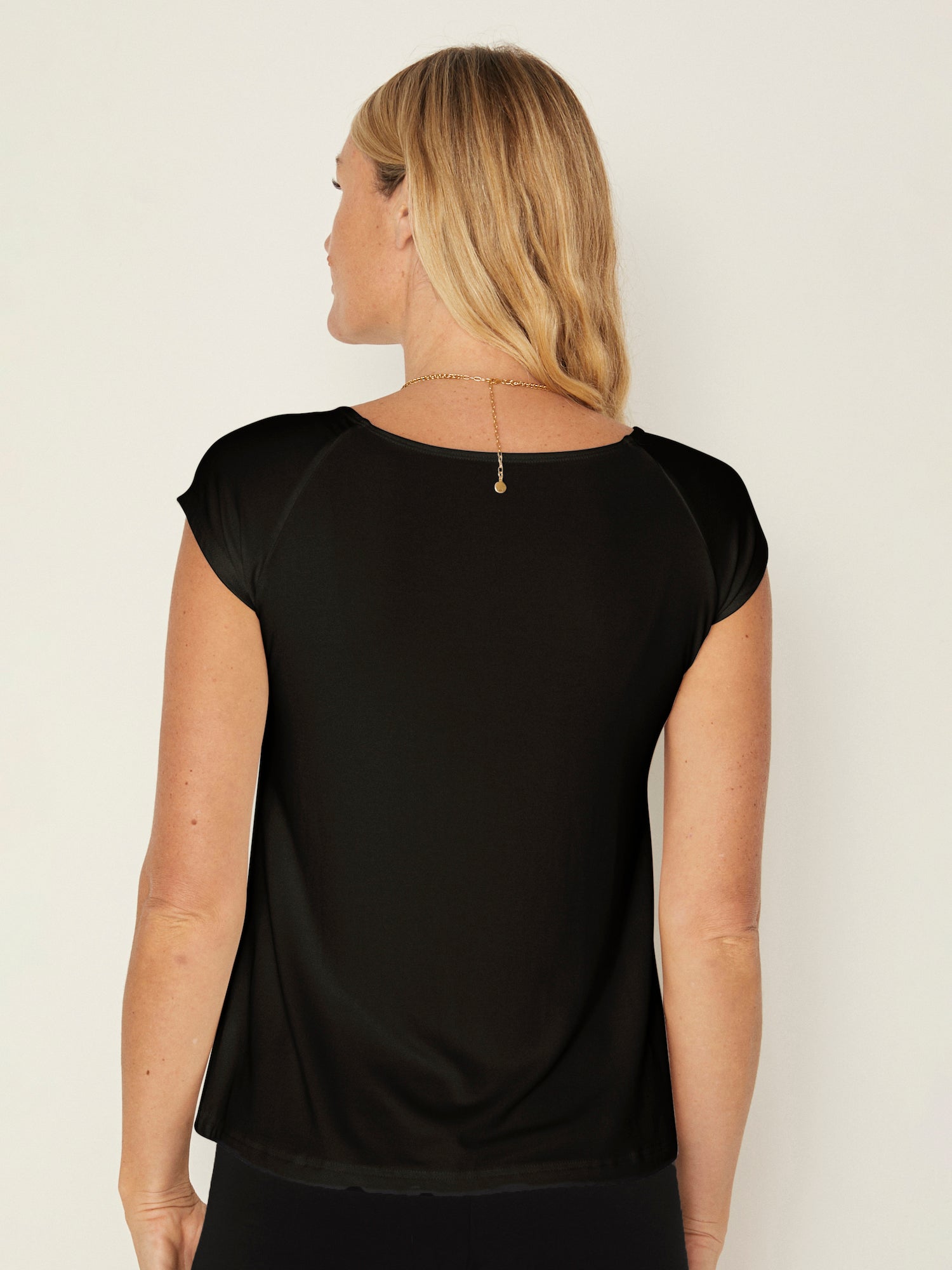 Model wearing a black boat neck t-shirt with capped sleeves, fitted through shoulders and chest with slight flare at waist, women's bamboo clothing
