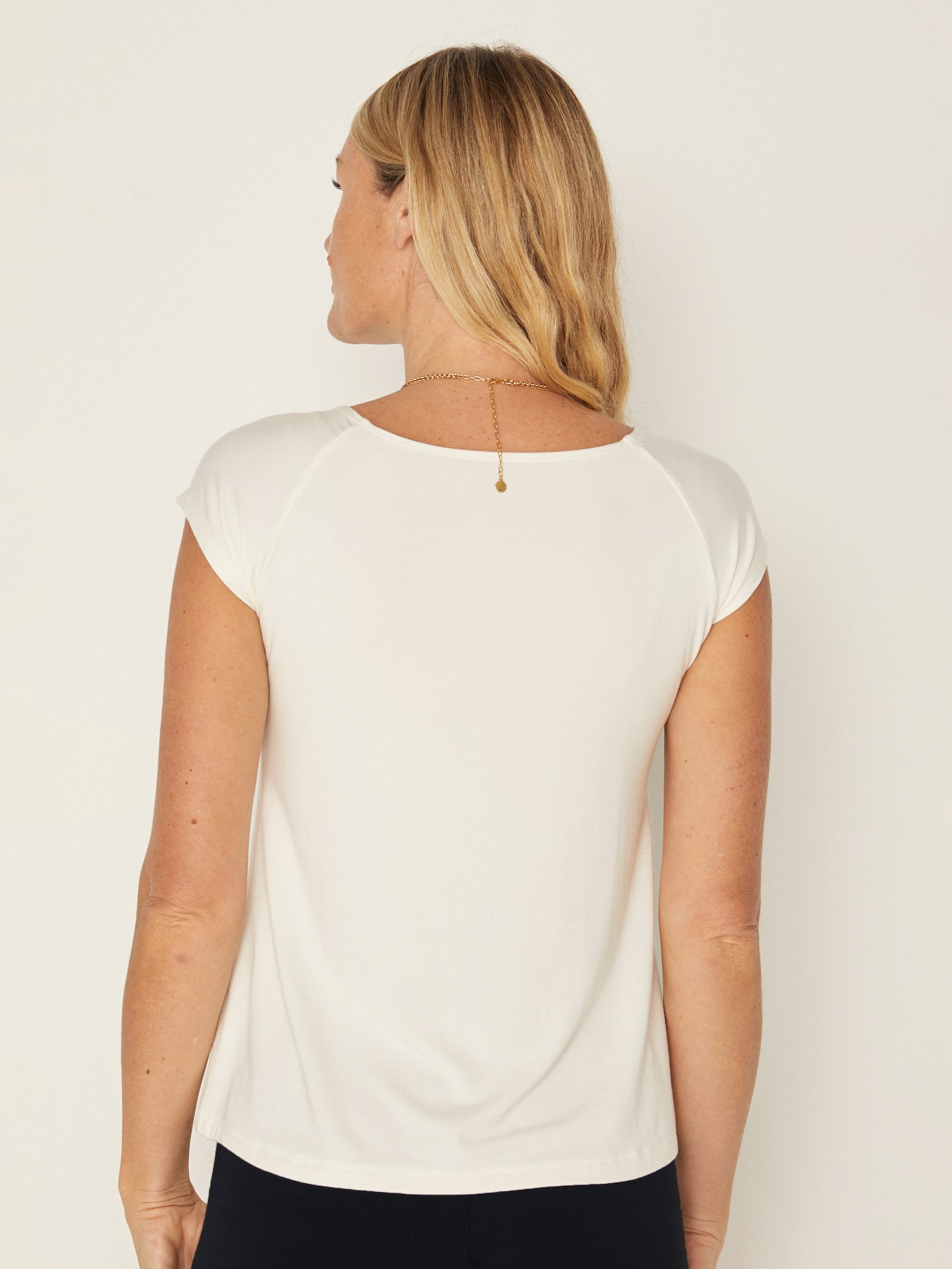 Model wearing a cream boat neck t-shirt with capped sleeves, fitted through shoulders and chest with loose fit to waist, women's bamboo clothing