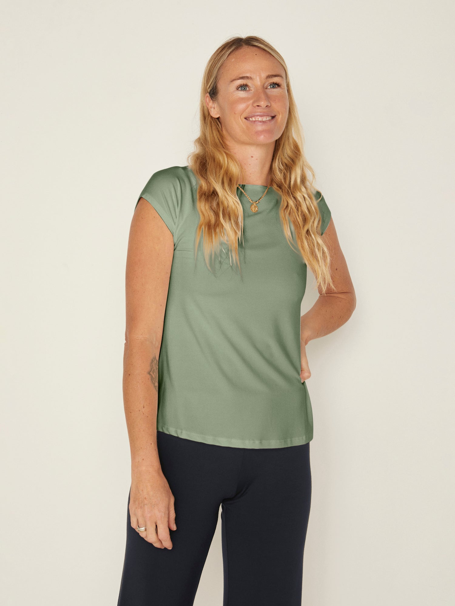 Model wearing a eucalyptus green boat neck t-shirt with capped sleeves, fitted through shoulders and chest with loose fit to waist, women's bamboo clothing