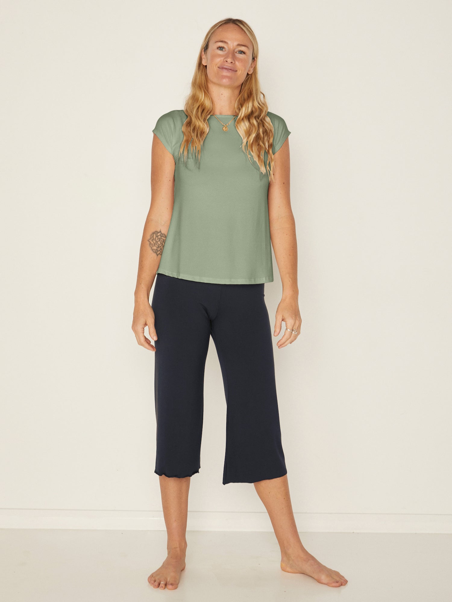 Model wearing a eucalyptus green boat neck t-shirt with capped sleeves, fitted through shoulders and chest with loose fit to waist, women's bamboo clothing