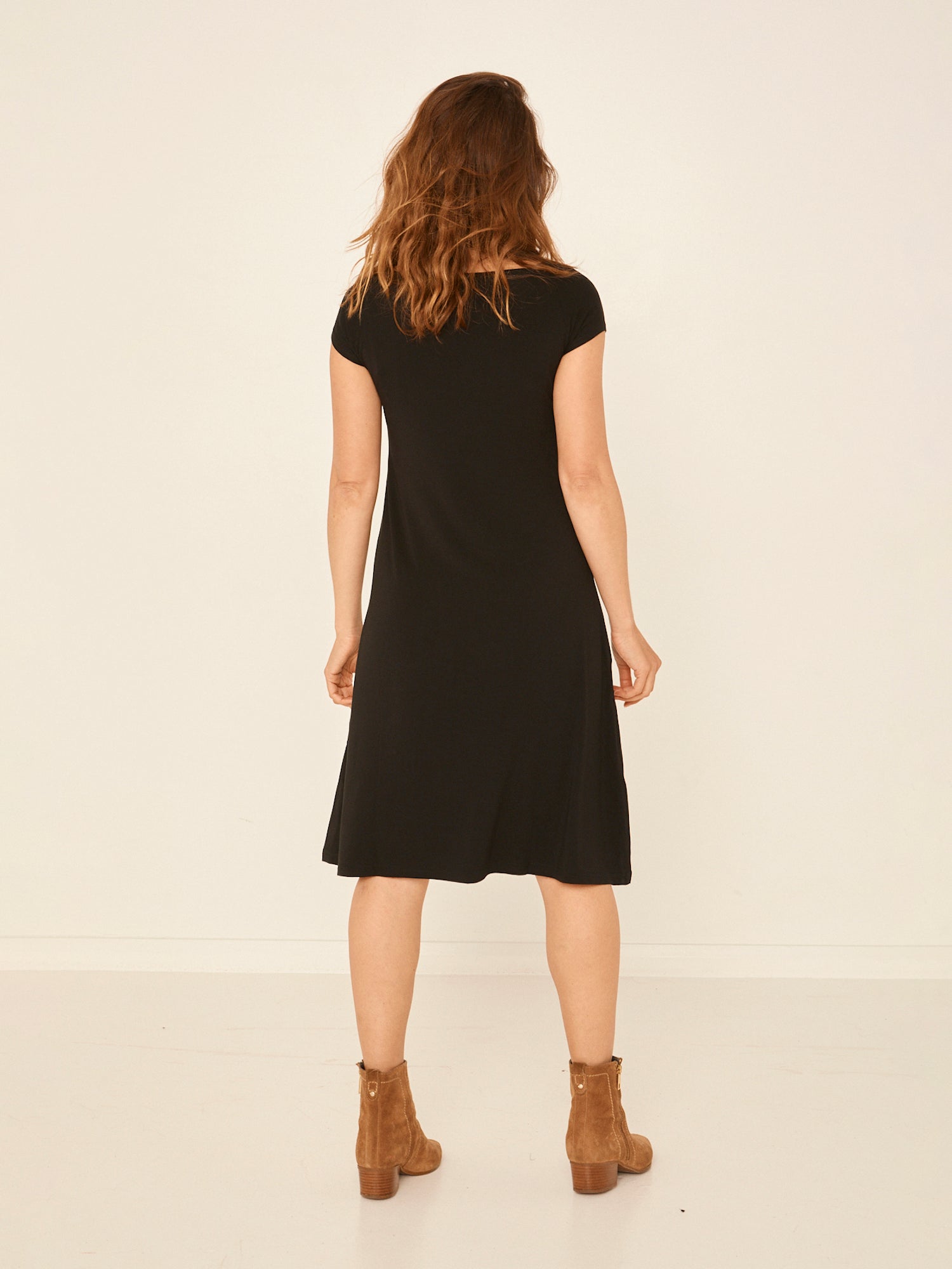 Model wearing a black boat neck dress with capped sleeves, fitted through shoulders and chest and a slight a-line flare to below the knee, women's bamboo clothing