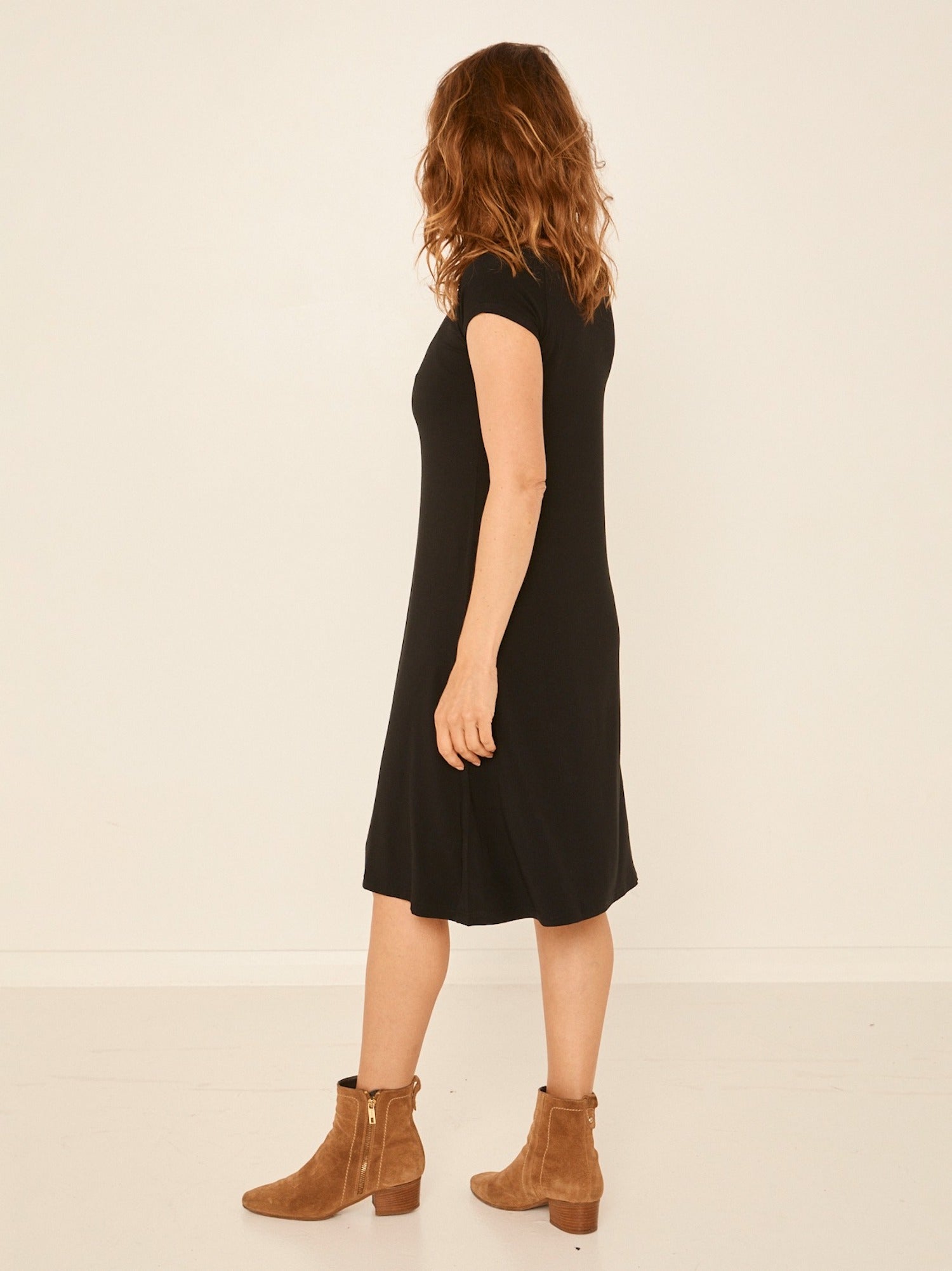 Model wearing a black boat neck dress with capped sleeves, fitted through shoulders and chest and a slight a-line flare to below the knee, women's bamboo clothing