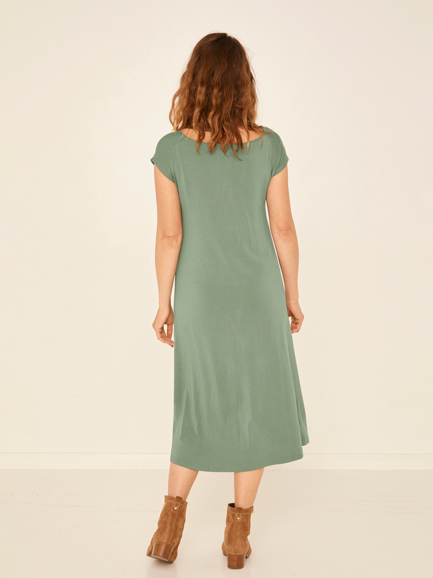 Model wearing a eucalyptus green boat neck dress with capped sleeves, fitted through shoulders and chest and a slight a-line flare to below the knee, women's bamboo clothing