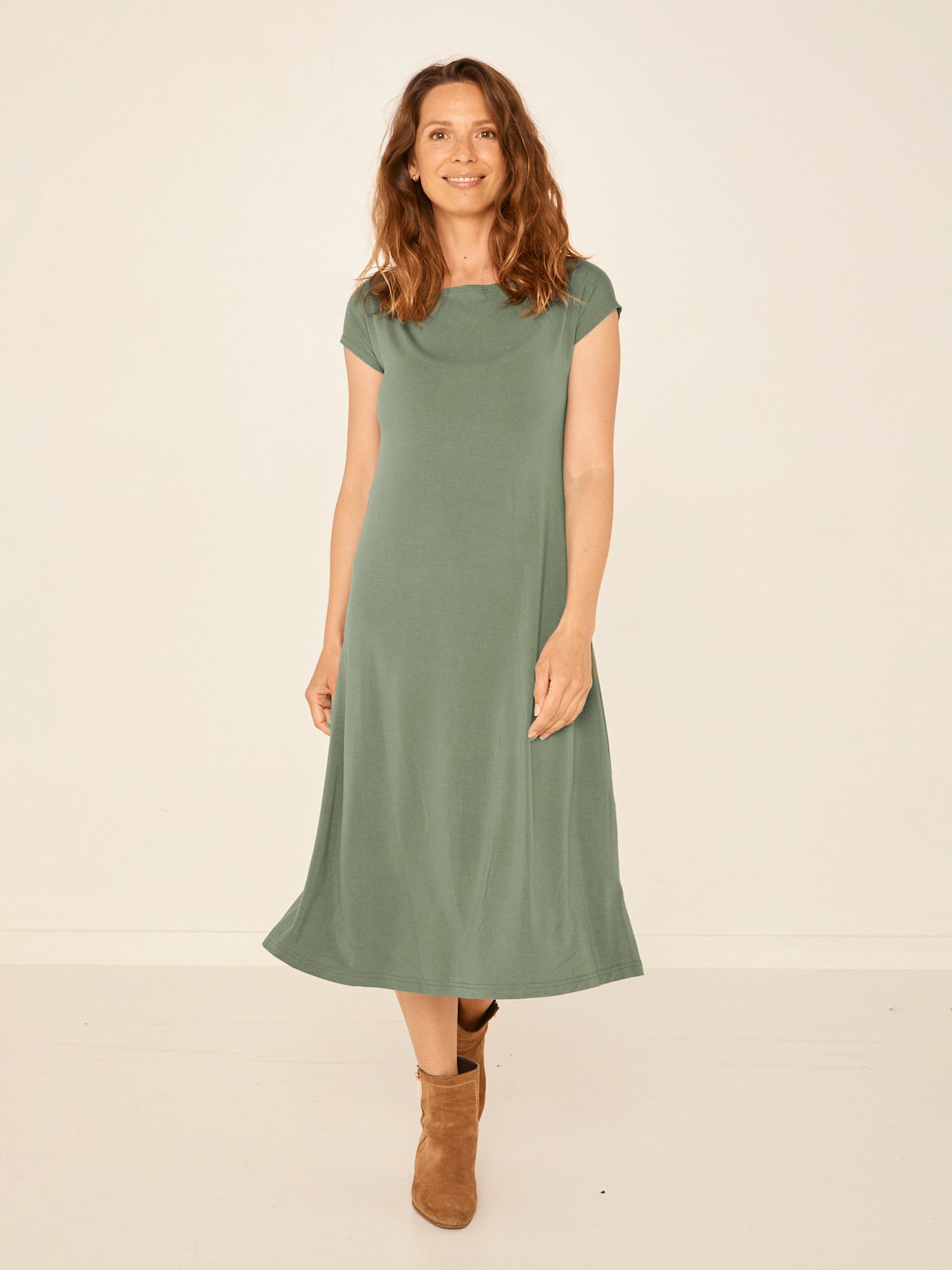 Model wearing a eucalyptus green boat neck dress with capped sleeves, fitted through shoulders and chest and a slight a-line flare to below the knee, women's bamboo clothing
