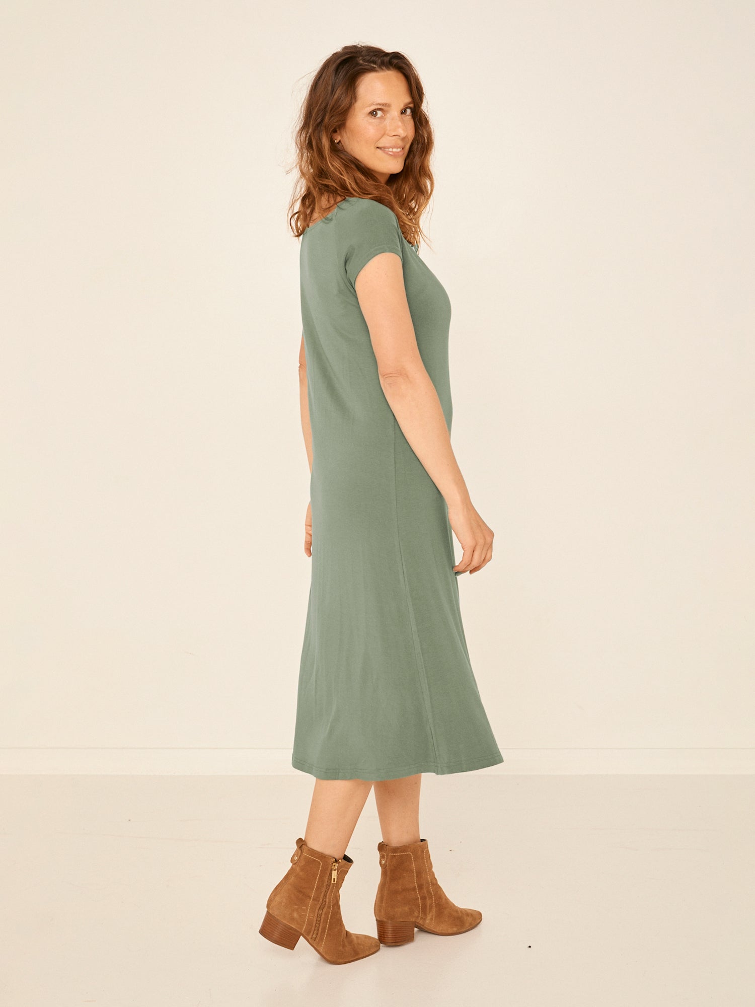 Model wearing a eucalyptus green boat neck dress with capped sleeves, fitted through shoulders and chest and a slight a-line flare to below the knee, women's bamboo clothing