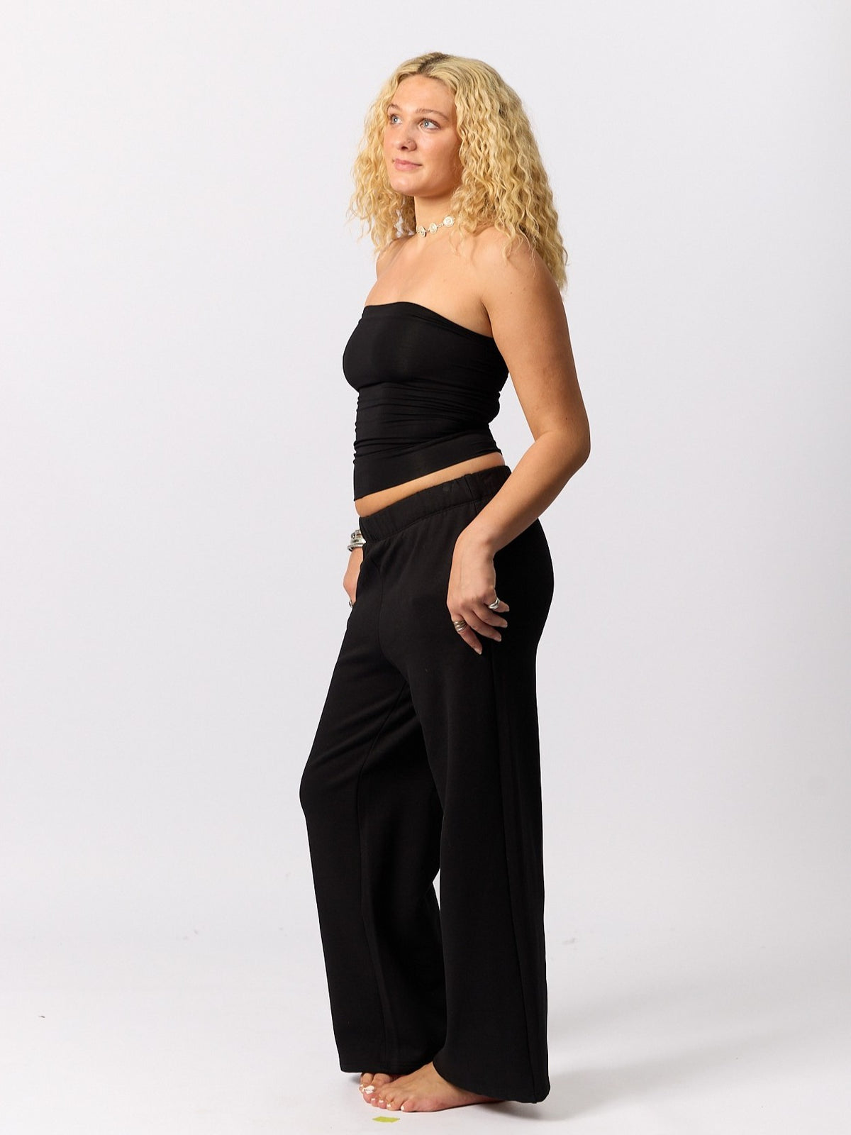 A woman modeling a black strapless crop top and matching wide-leg pants against a plain white studio background.