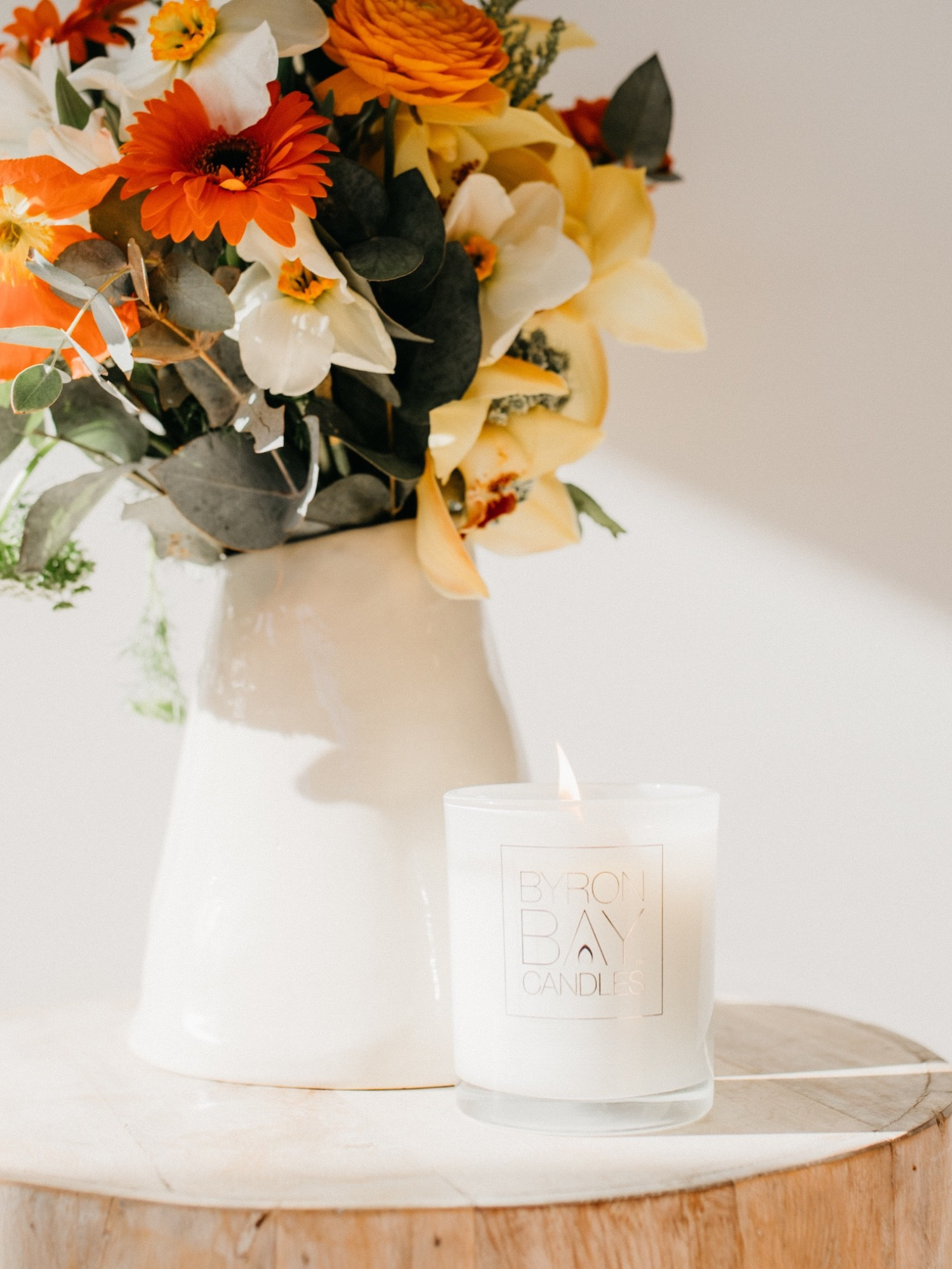 Byron Bay harmony essential oil candle with a floral arrangement in a vase on a wooden surface