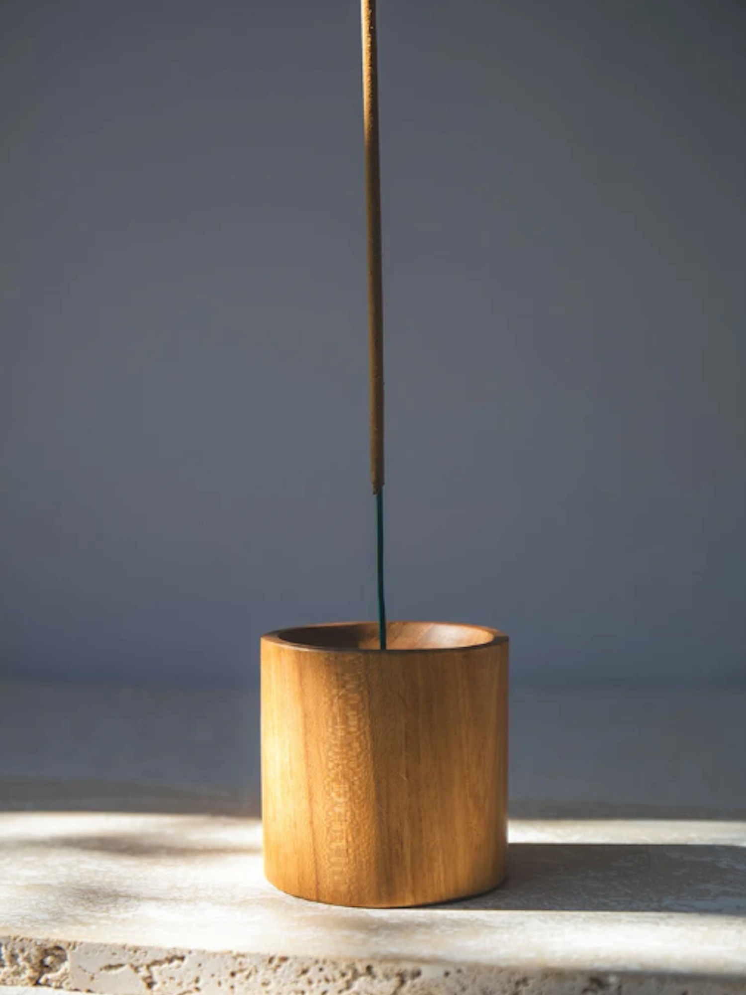Wooden cylindrical incense holder with a single stick of incense on a grey background