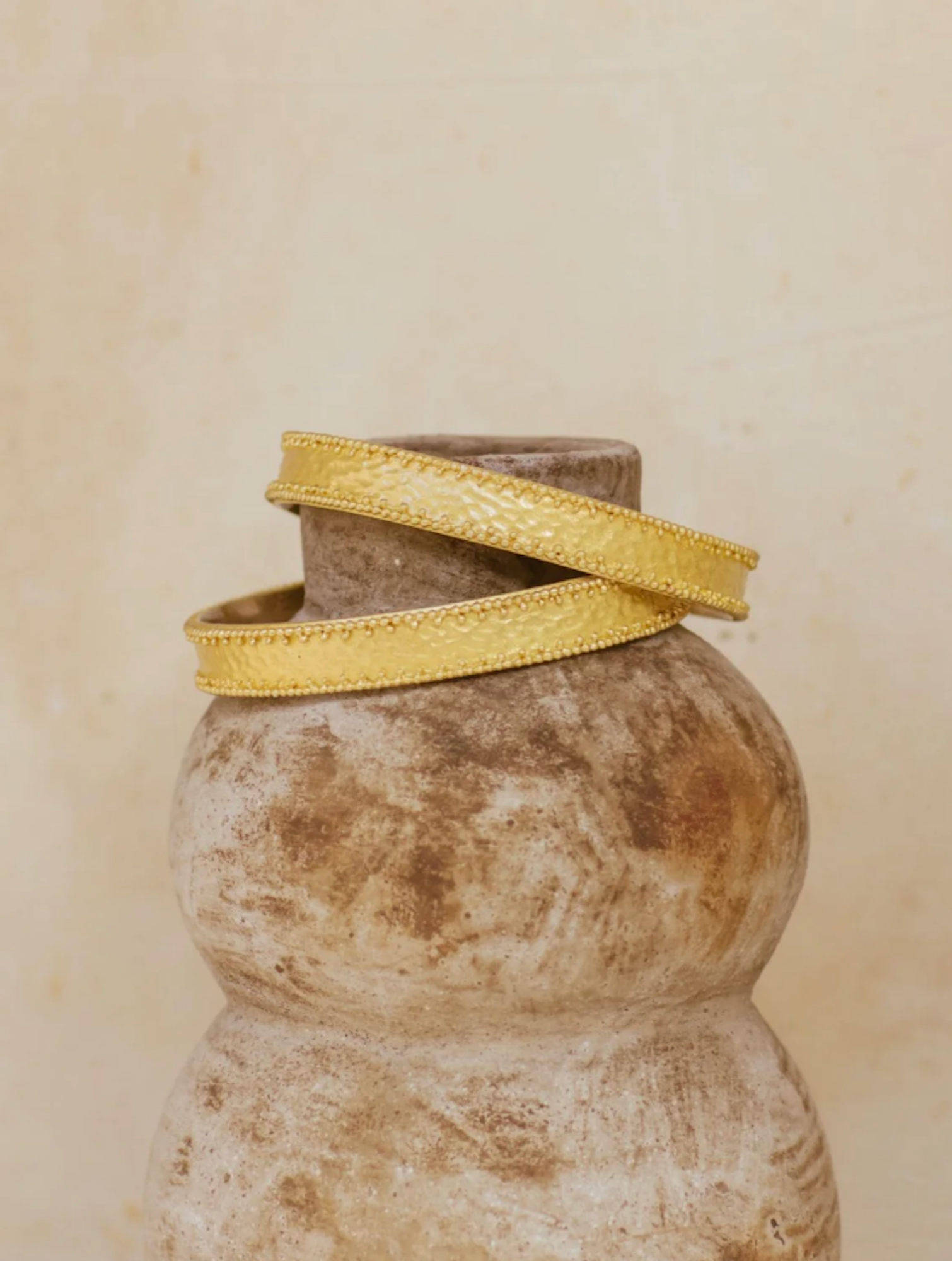 Brass bangles on a textured vase against a beige background