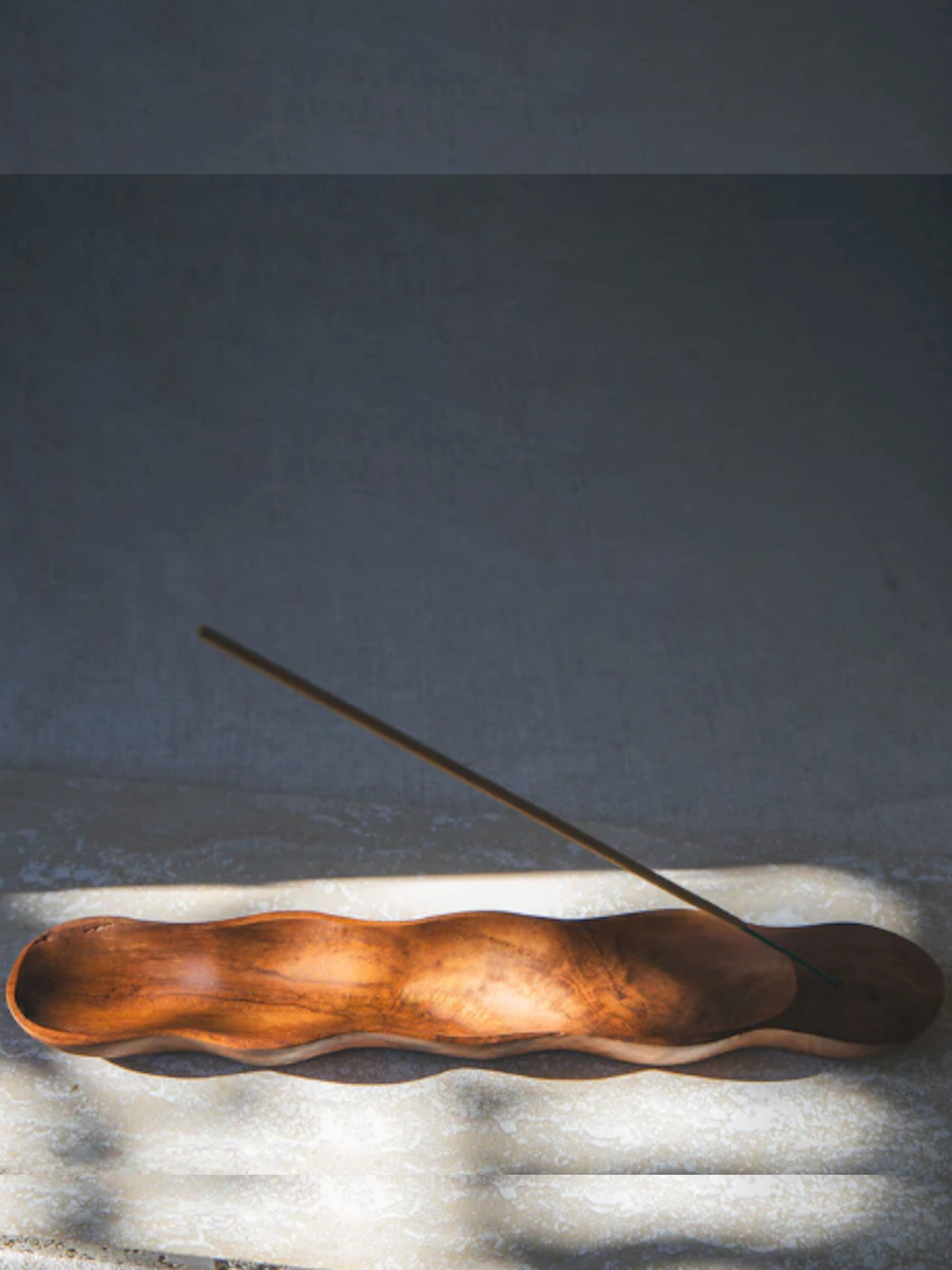 Wooden incense holder with a single incense stick on a textured surface with a dark background