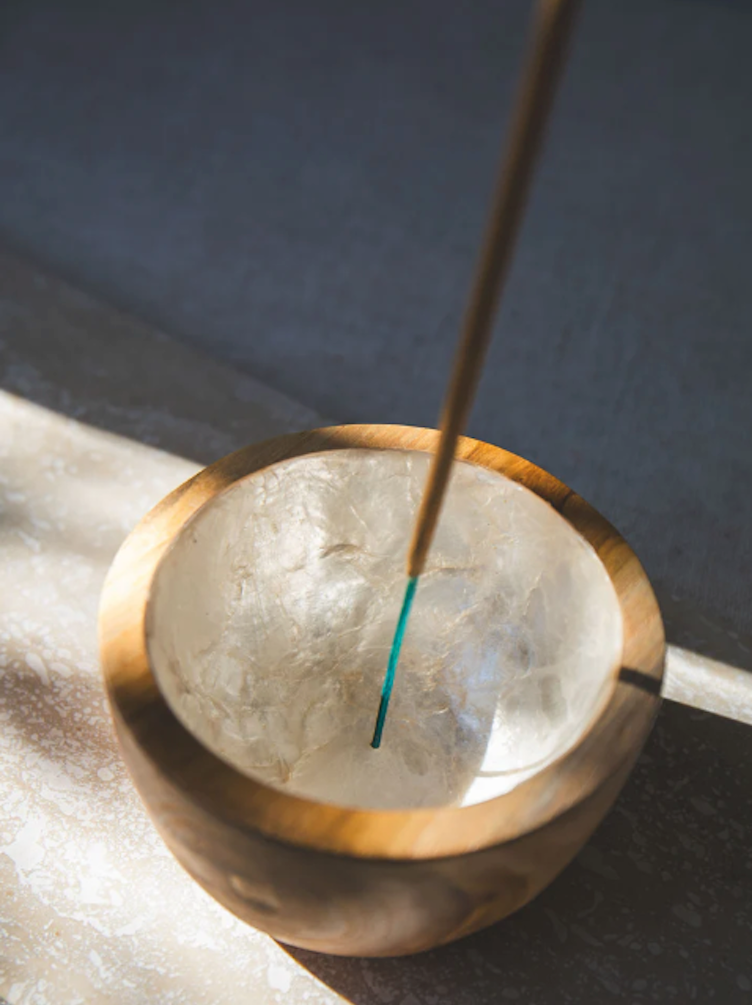 Incense stick in a decorative teak wood and shell holder with a textured surface