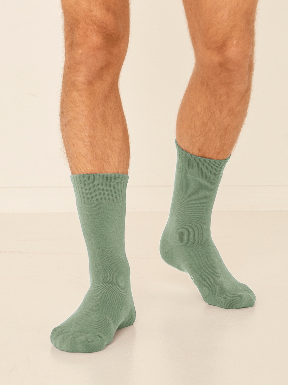Model wearing eucalyptus green mid rise thick work, hiking, bed socks with ribbed top and thick cushioned sole, bamboo socks
