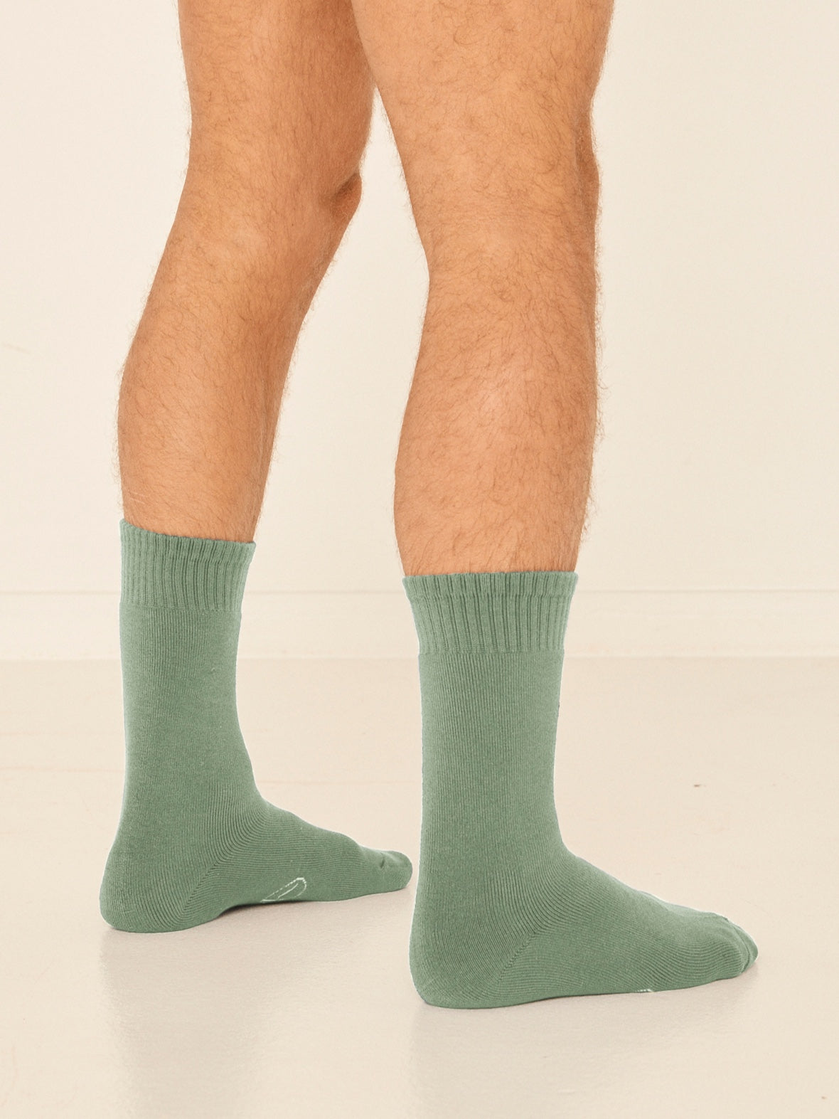 Model wearing eucalyptus green mid rise thick work, hiking, bed socks with ribbed top and thick cushioned sole, bamboo socks