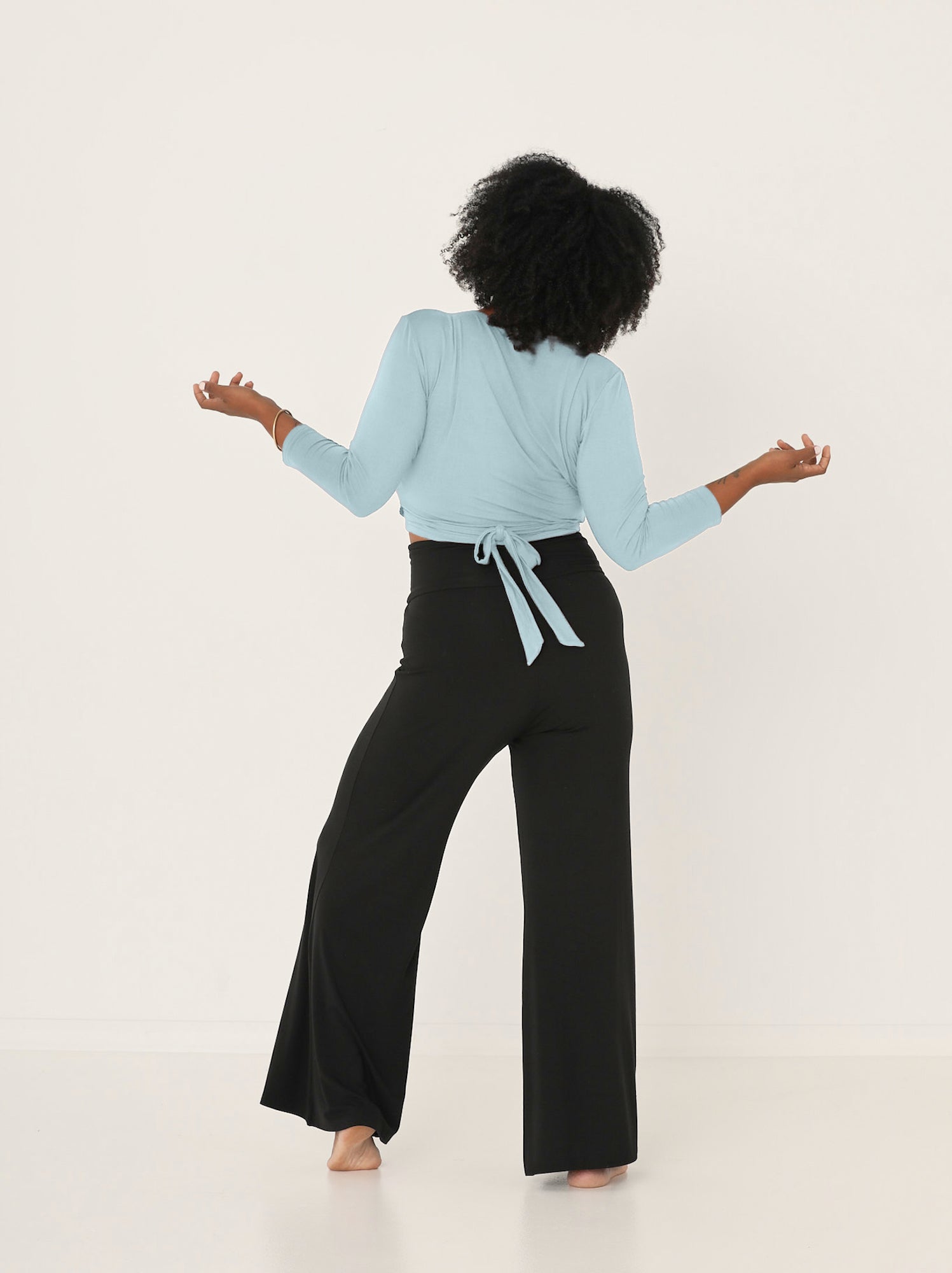 Woman wearing Bamboo light topaz blue wrap cardigan top with a tie detail and black wide leg palazzo pants on a white background