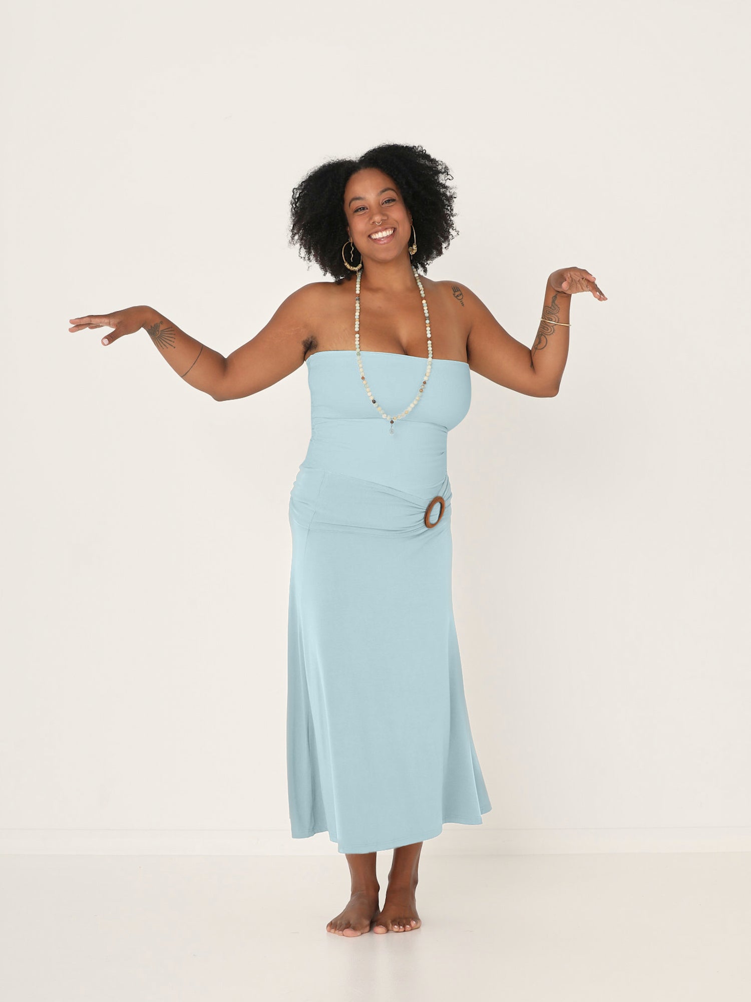 model wearing a bamboo light topaz blue tube top, flat fabric belt with a brown circular wooden buckle and a topaz blue swishy skirt on a white background