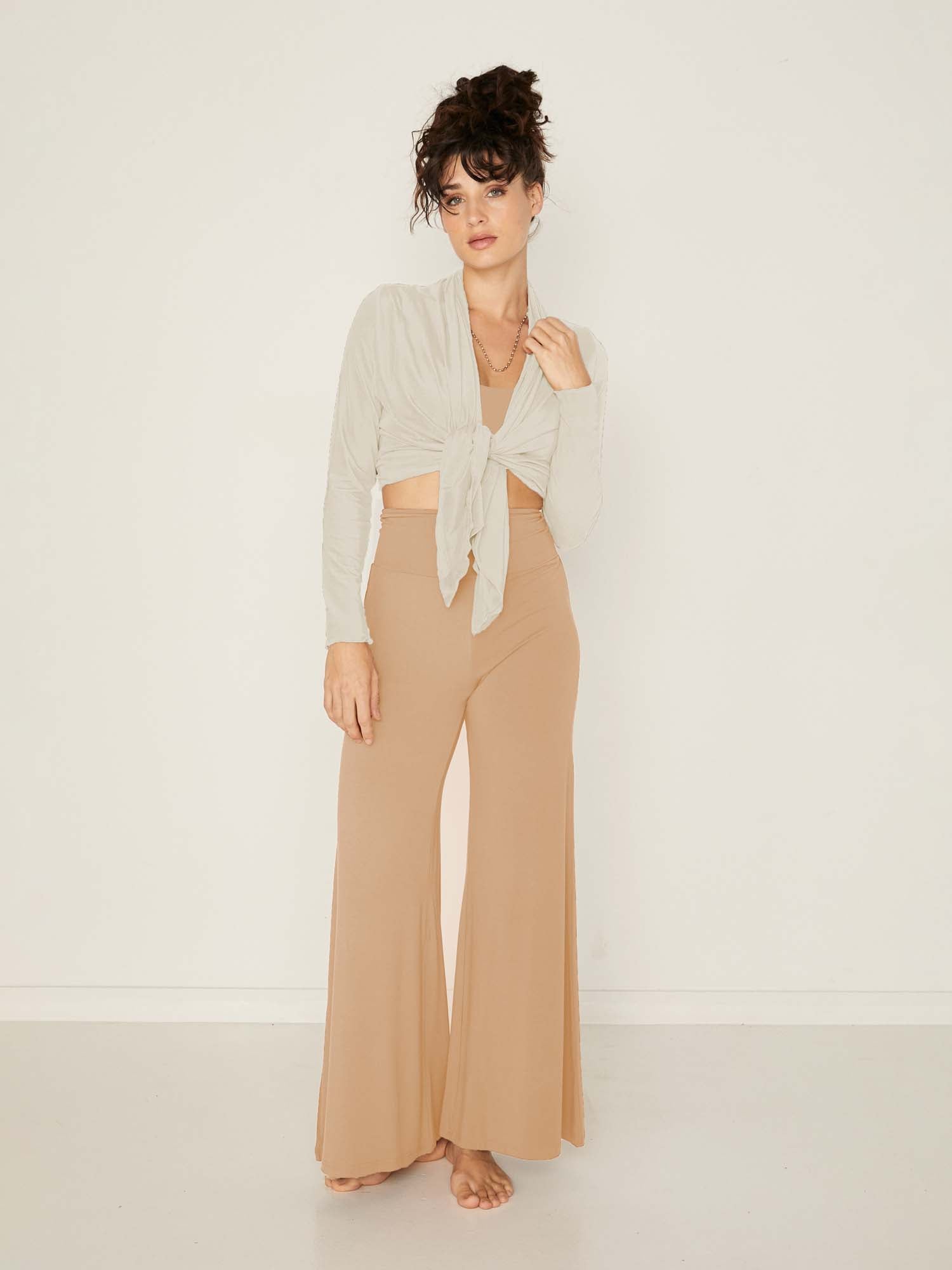Model wearing caramel full length palazzo pants, fitted waist and hips with flowing wide leg, adjustible high waistband, women's bamboo clothing
