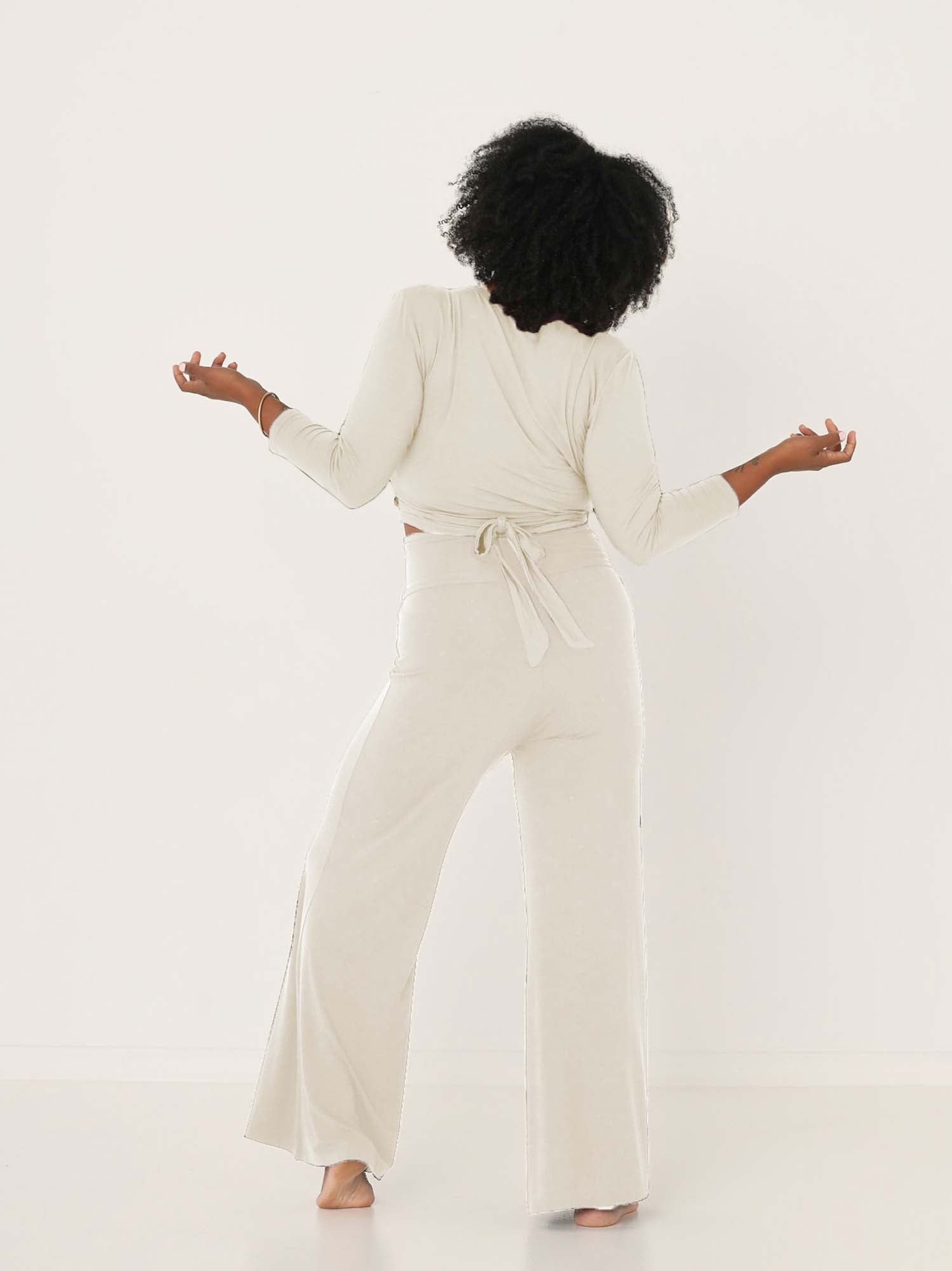 Model wearing cream full length palazzo pants, fitted waist and hips with flowing wide leg, adjustible high waistband, women's bamboo clothing