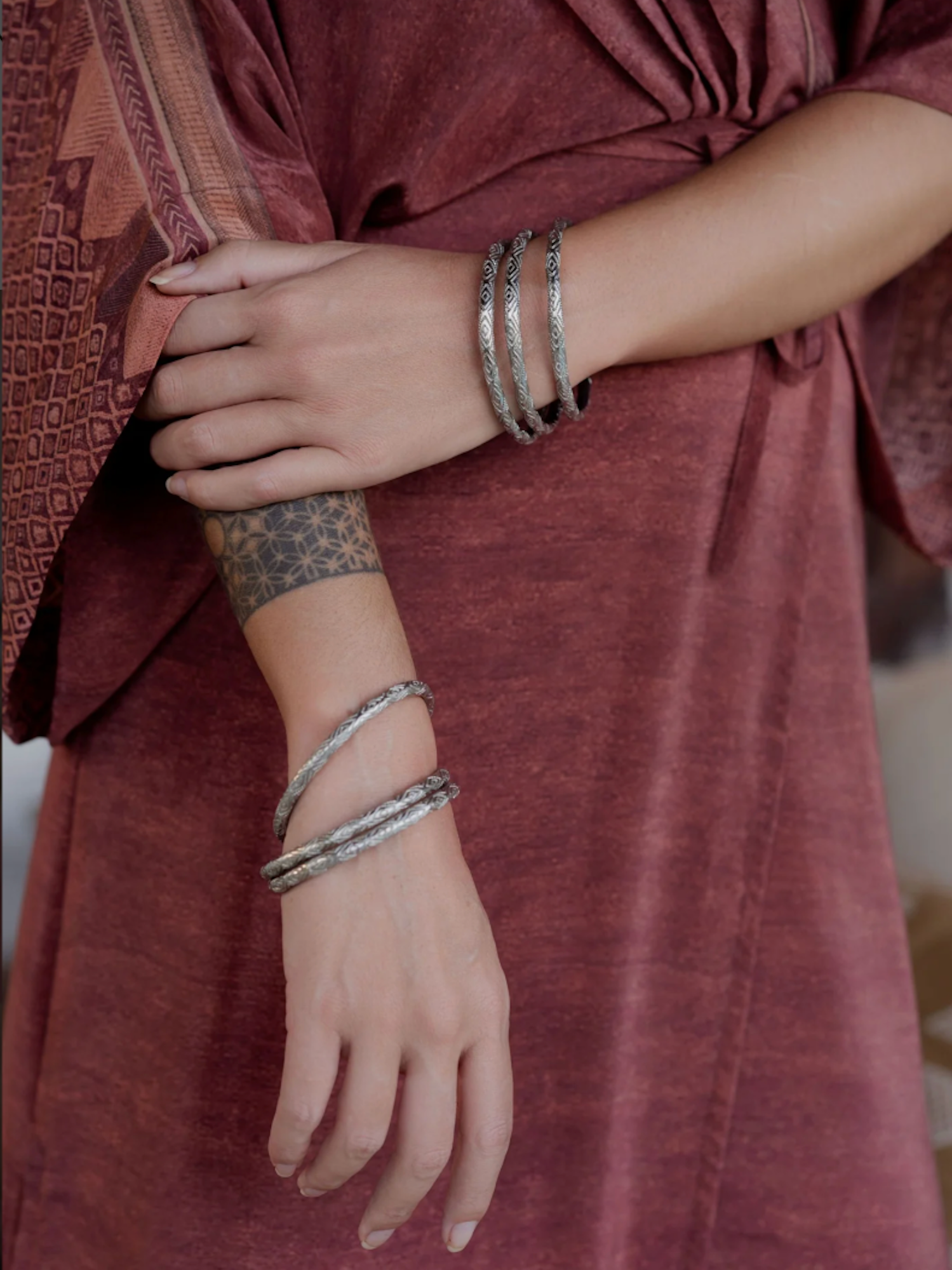 Person wearing multiple silver bangles on a maroon garment