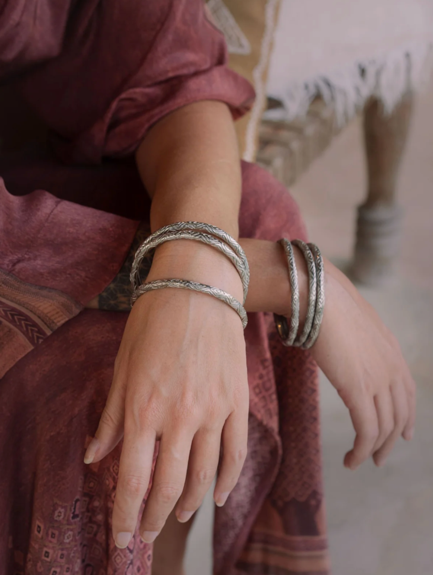 Close-up of a person's wrist wearing multiple silver bracelets with a blurred background.