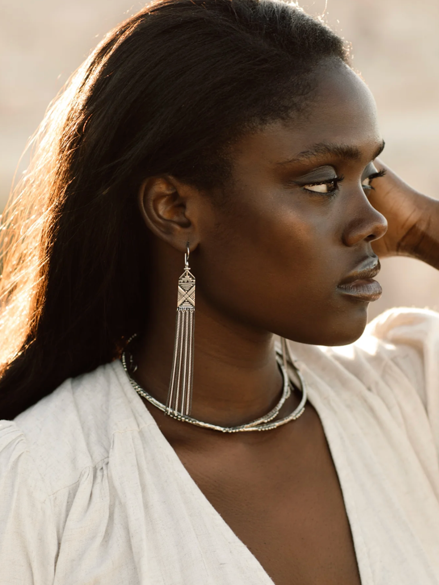 Woman wearing a silver earring and necklace against a neutral background
