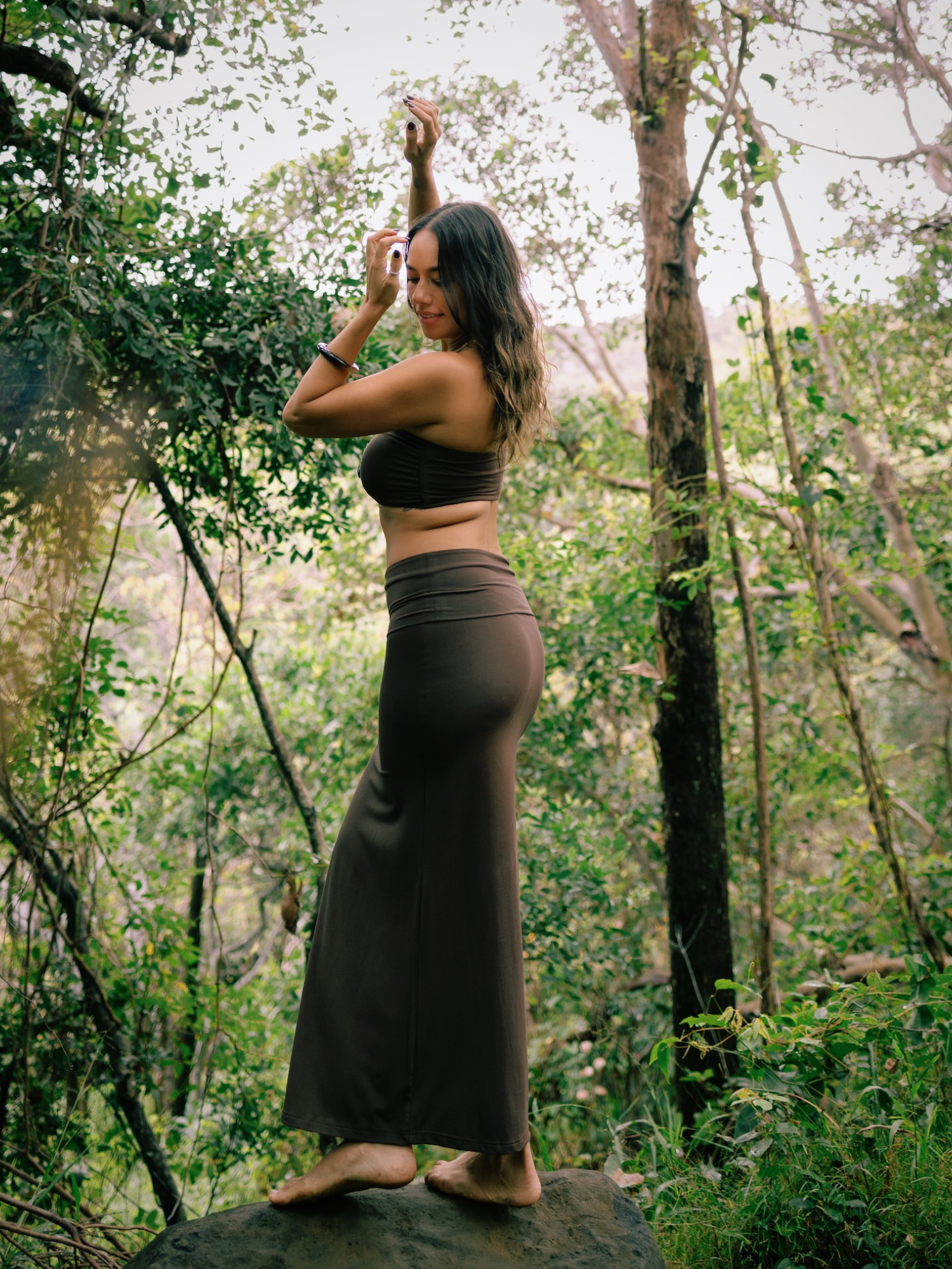 Woman in a cocoa brown bamboo maxi skirt standing on a rock in a forest