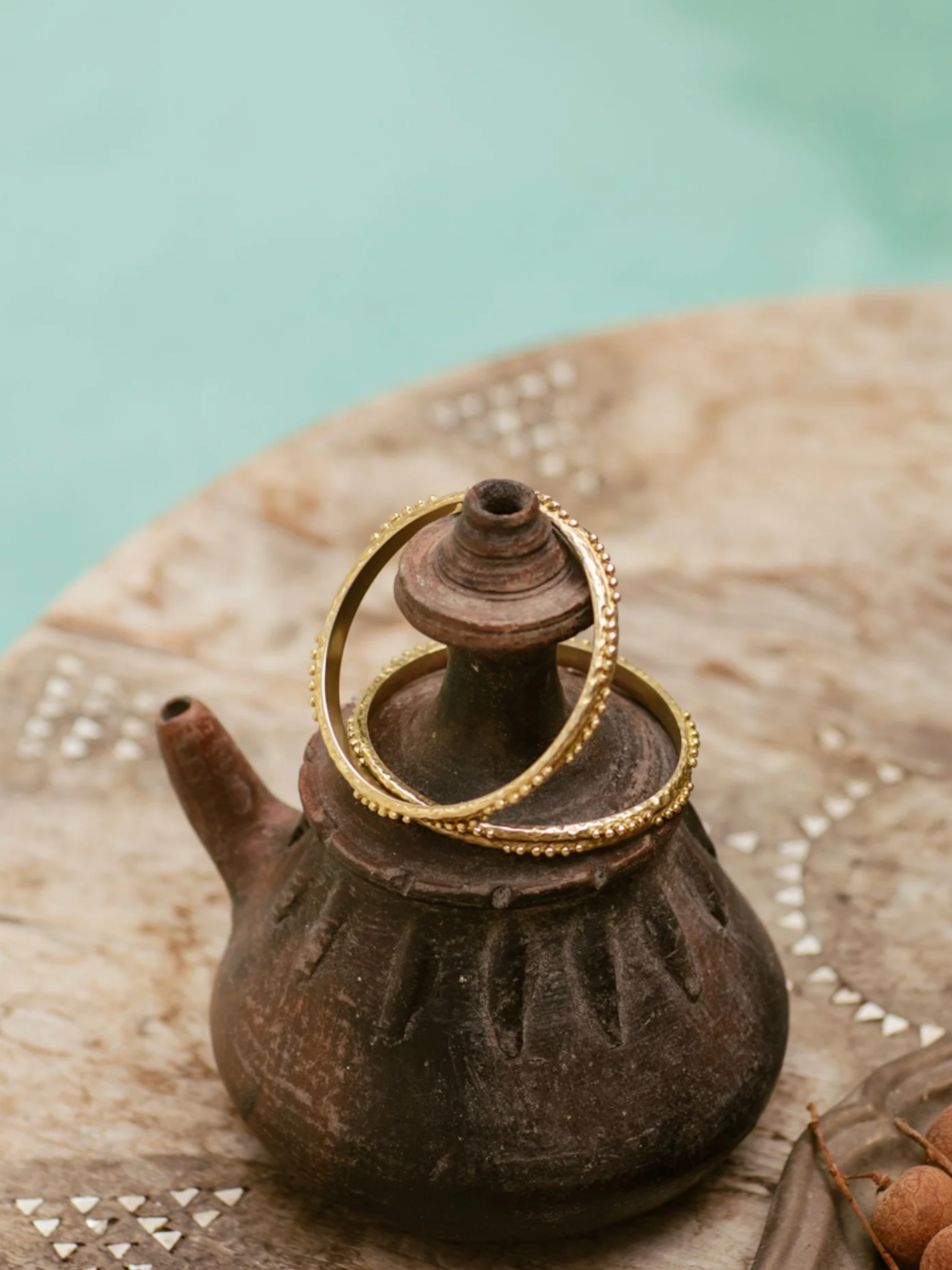 Ceramic teapot with a 2 brass bangles on top against a light blue background