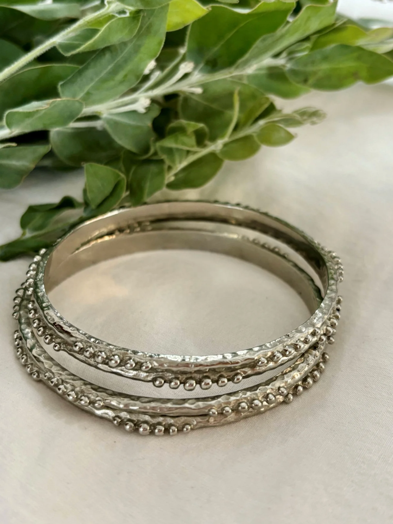Stack of silver bangles on a light surface with green leaves in the background