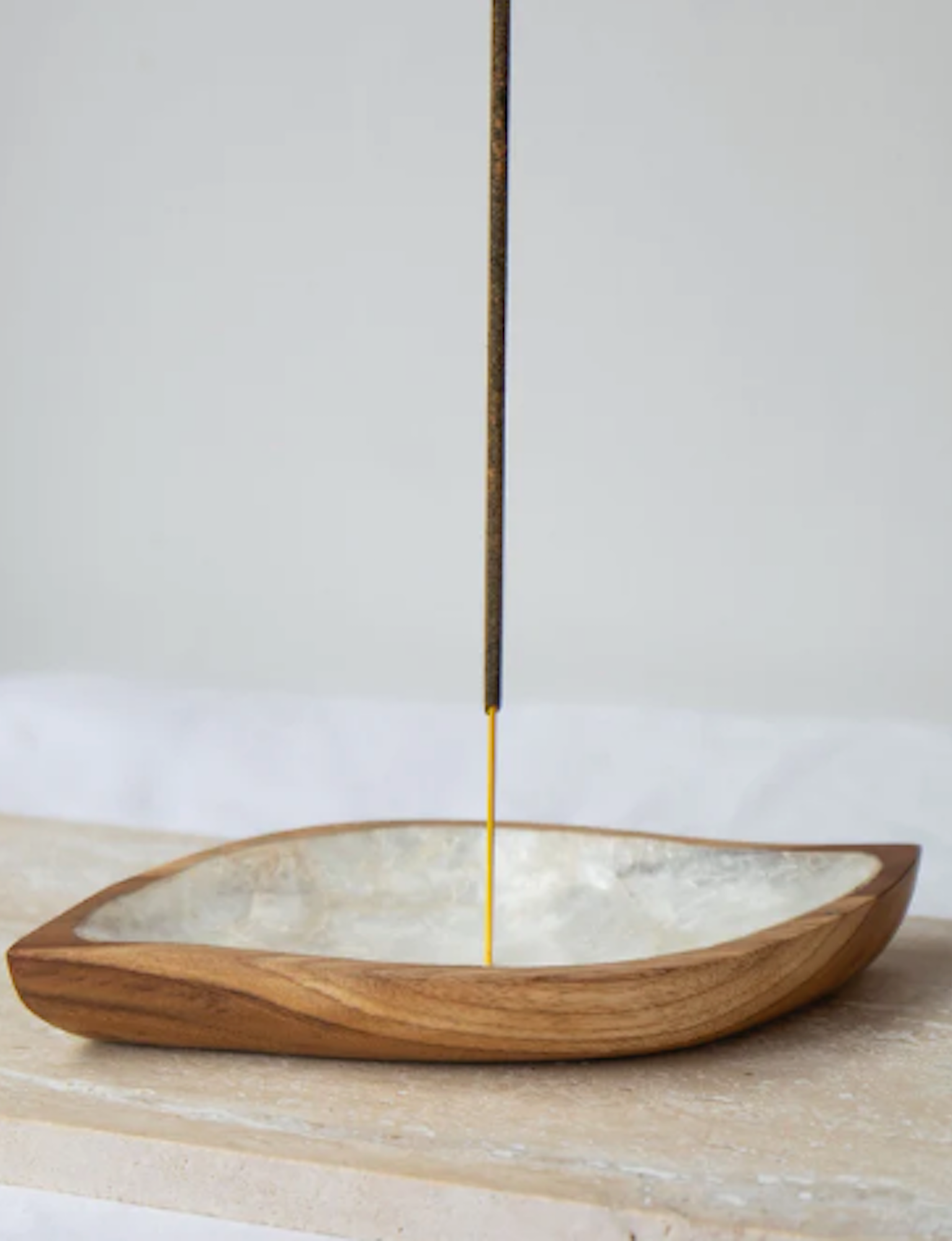 Incense stick in a shell lined wooden holder on a neutral background