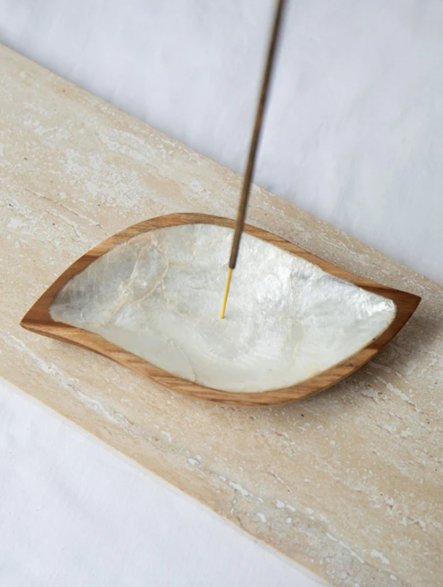 Incense stick in a shell lined wooden holder on a neutral background