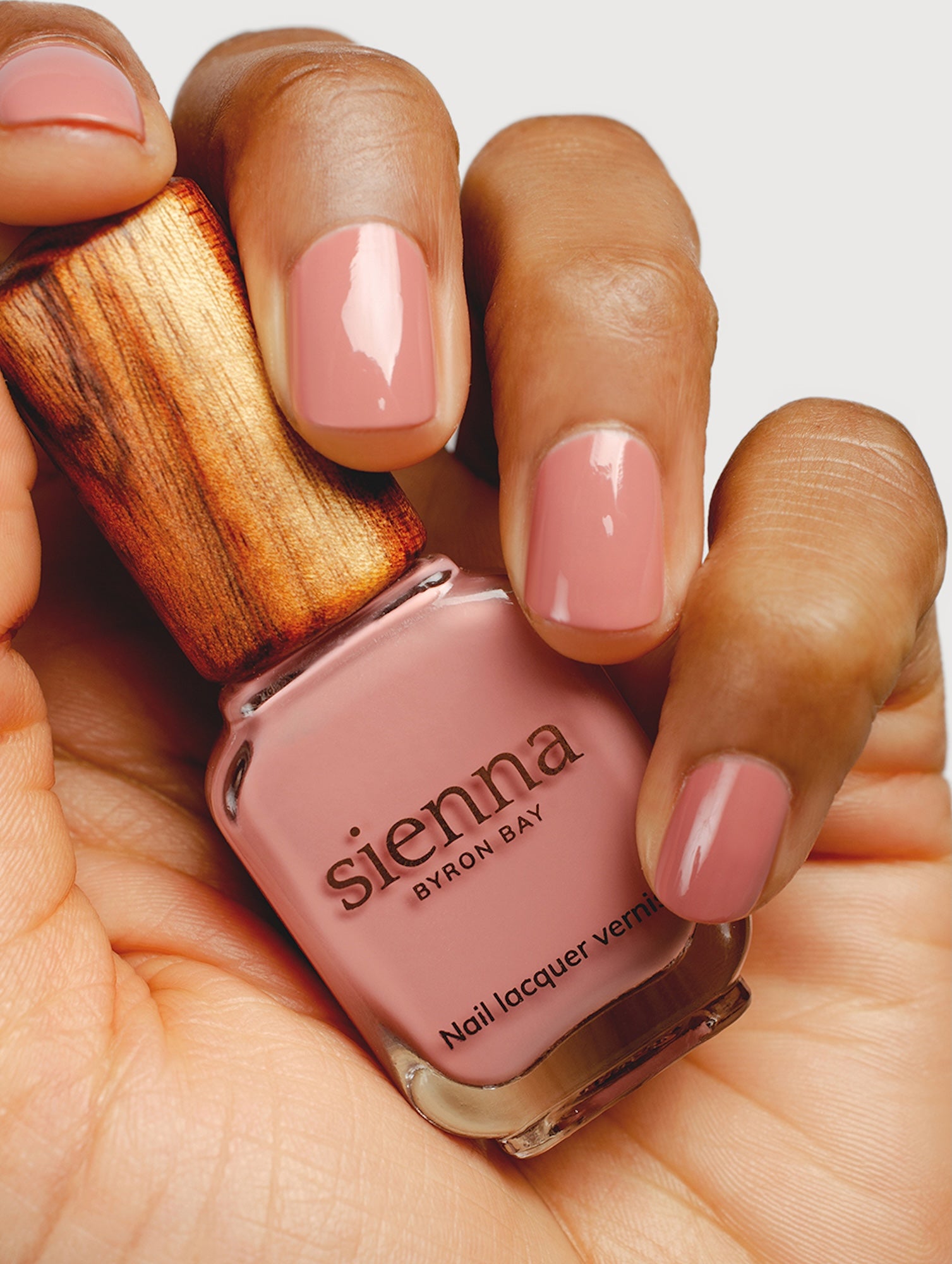 Hand holding a bottle of Sienna Byron Bay nail polish with matching pink nails.