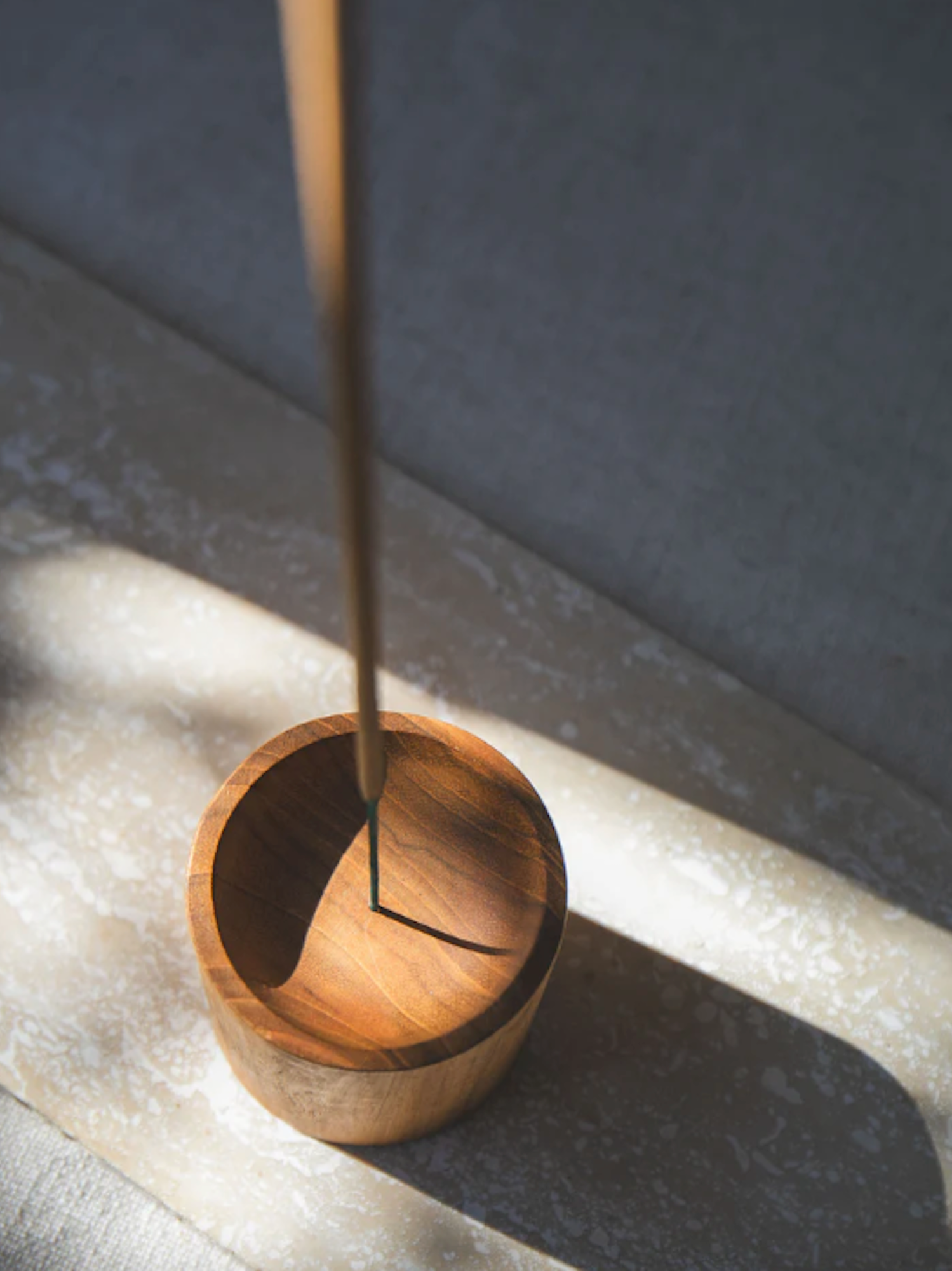Wooden incense holder with a single incense stick on a reflective surface.